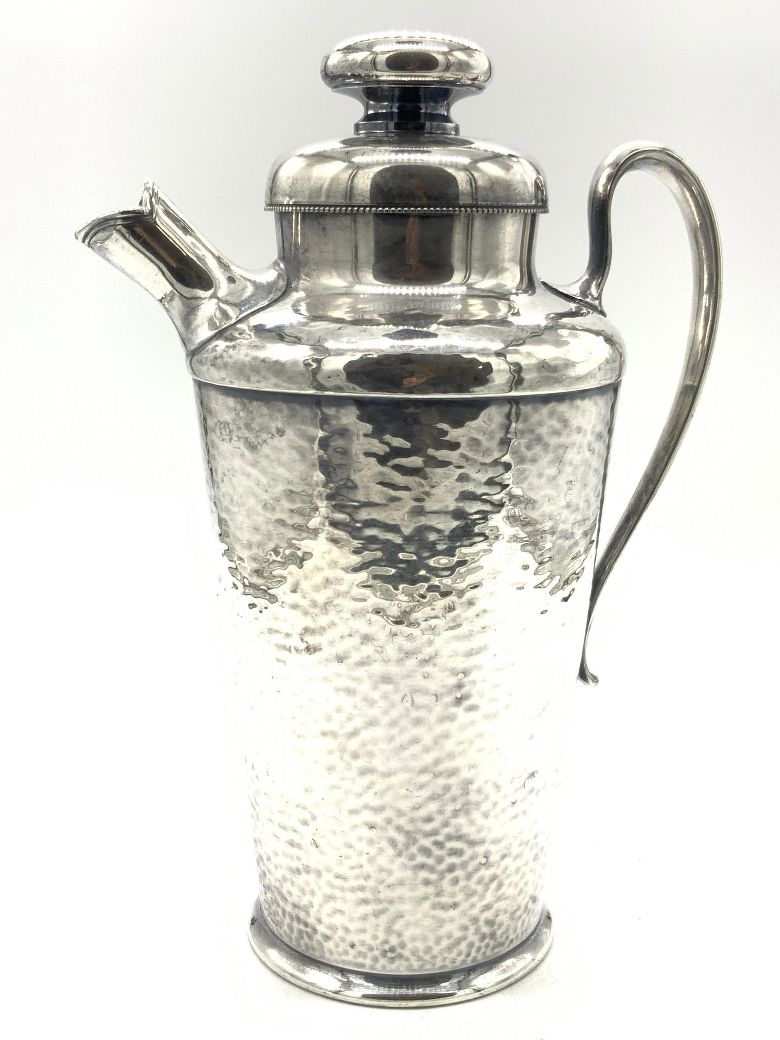 MERDIDENS.P.C.O. Hammered Metal Cocktail Pitcher: Hammered white metal pitcher with side handle and spout. Lid is corked on inside. Approximately 10.25 inches tall and marked on underside MERDIDENS.P.C.O. International SCO. 313. Minor wearing to exte