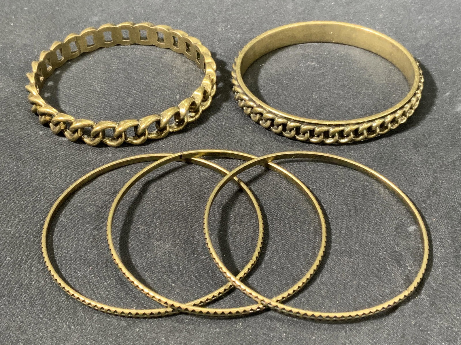 Lot 5 Brass Tone Etched & Cable Link Bangles: Lot of 5 brass tone bangles. 3 thin band bangles with geometric etched motif and 2 thicker banded bangles with cable chain motifs. All bangles measure approx. 2.5 inches wide. In good condition, some 