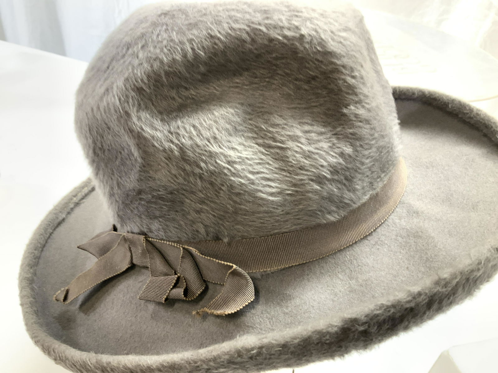 DUTCHESS Fabric Hat in Bergdorf Goodman Box, Italy: Total 2. Plush grey fabric hat, size Medium , signed ‘ Dutchess Body Made in Italy’ , has tie strings, rounded brim ( 2.5 in) and ribbed fabric bow. Comes in a silver Bergdorf Goodman hat box. Hat