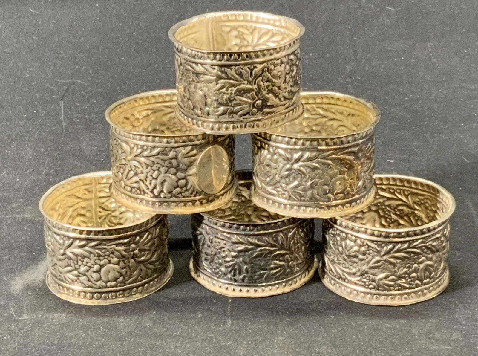 Set 6 Vintage Embossed Metal Napkin Rings: Set of 6 ornate embossed metal napkin rings with flora motifs. Possibly silver plates. Surface wear consistent with age and exposure. Measure approx. 2 inches diameter. Napkin ring, napkin ring set, m
