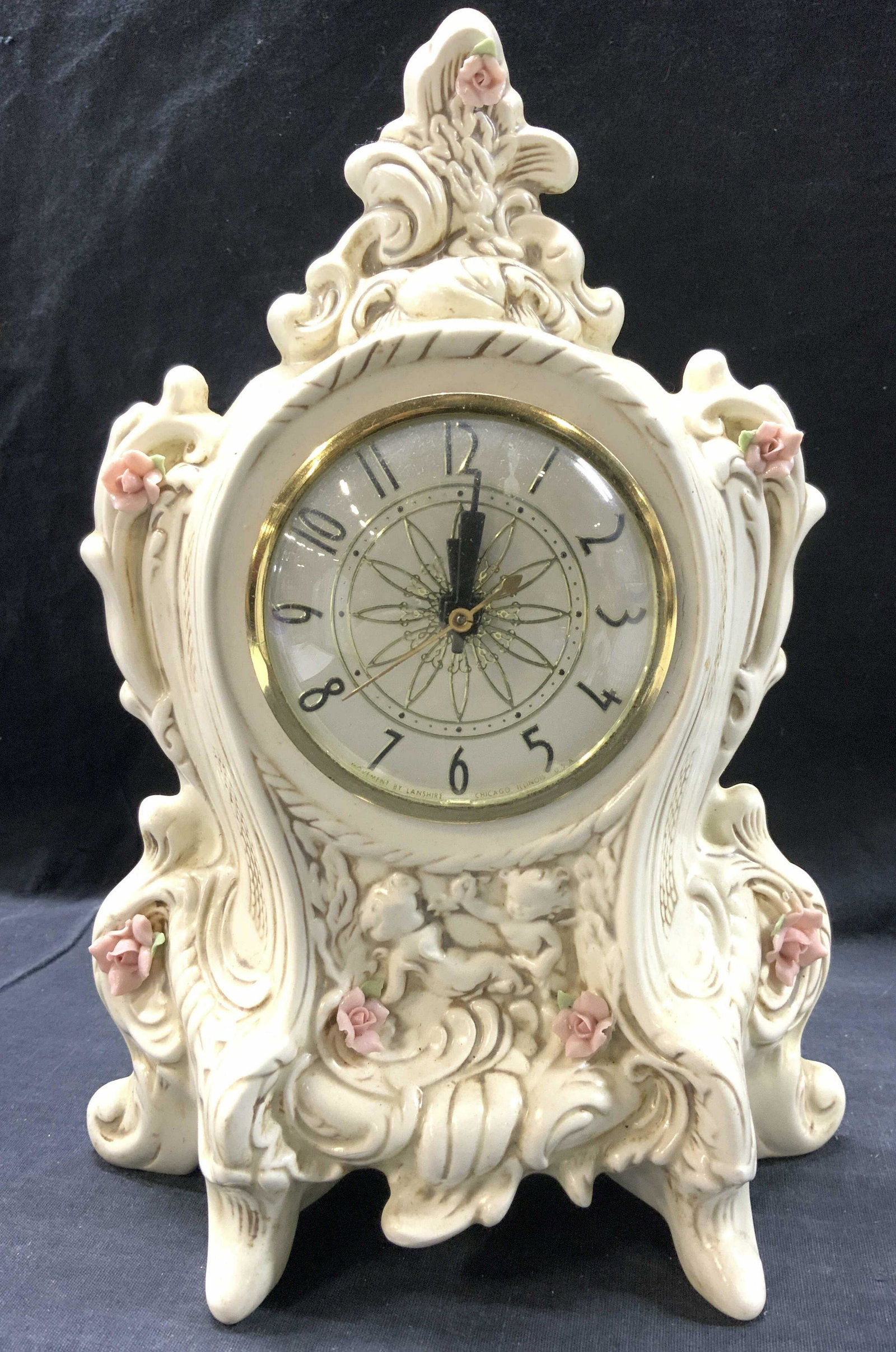 MOVEMENT BY LANSHIRE Vinatge Ornate Footed Clock: Clock face reads MOVEMENT BY LANSHIRE. Piece is cream toned & has ornately detailed structures in addition to floral & leaf detail. Piece measures approx 11 inches tall 8 inches wide. MOVEMENT BY LANS