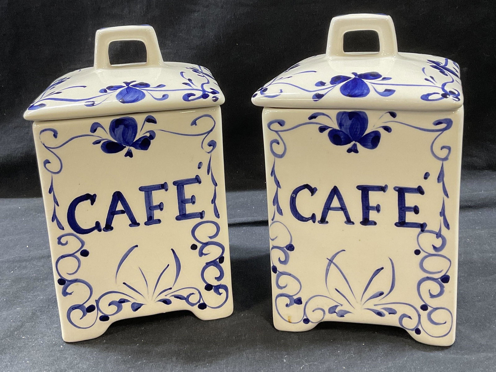 Pair Jay Willfred Porcelain Cannisters, Portugal: 2 Lidded Porcelain Cafe Containers. Labeled on bottom Made in Portugal, Jay Willfred. Porcelain is painted with blue detail and labeled with CAFE. Measures approx 8H x 4.5 inches. Minor wear to pieces