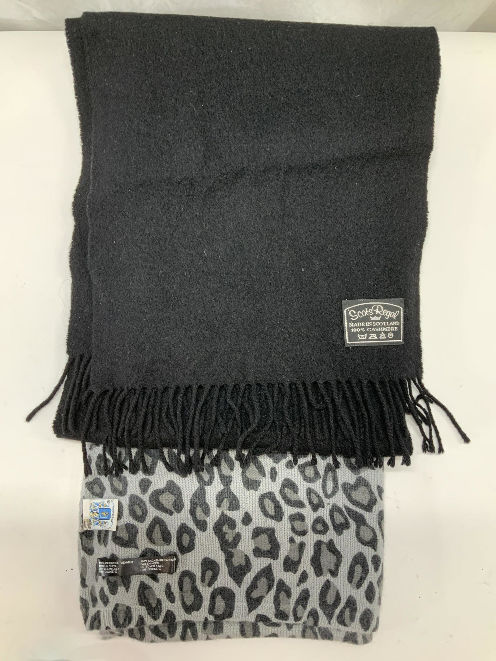 Lot 2 Cashmere Scarves, Animal Print Scotland More: Regal Scot Labeled Black cashmere scarf with end tassels. Made in Scotland. 11.5 x 57 in. Grey and black animal print scarf, label reads Portolano. Cashmere pashmina. Measures 22 x 78 in. Some blemish
