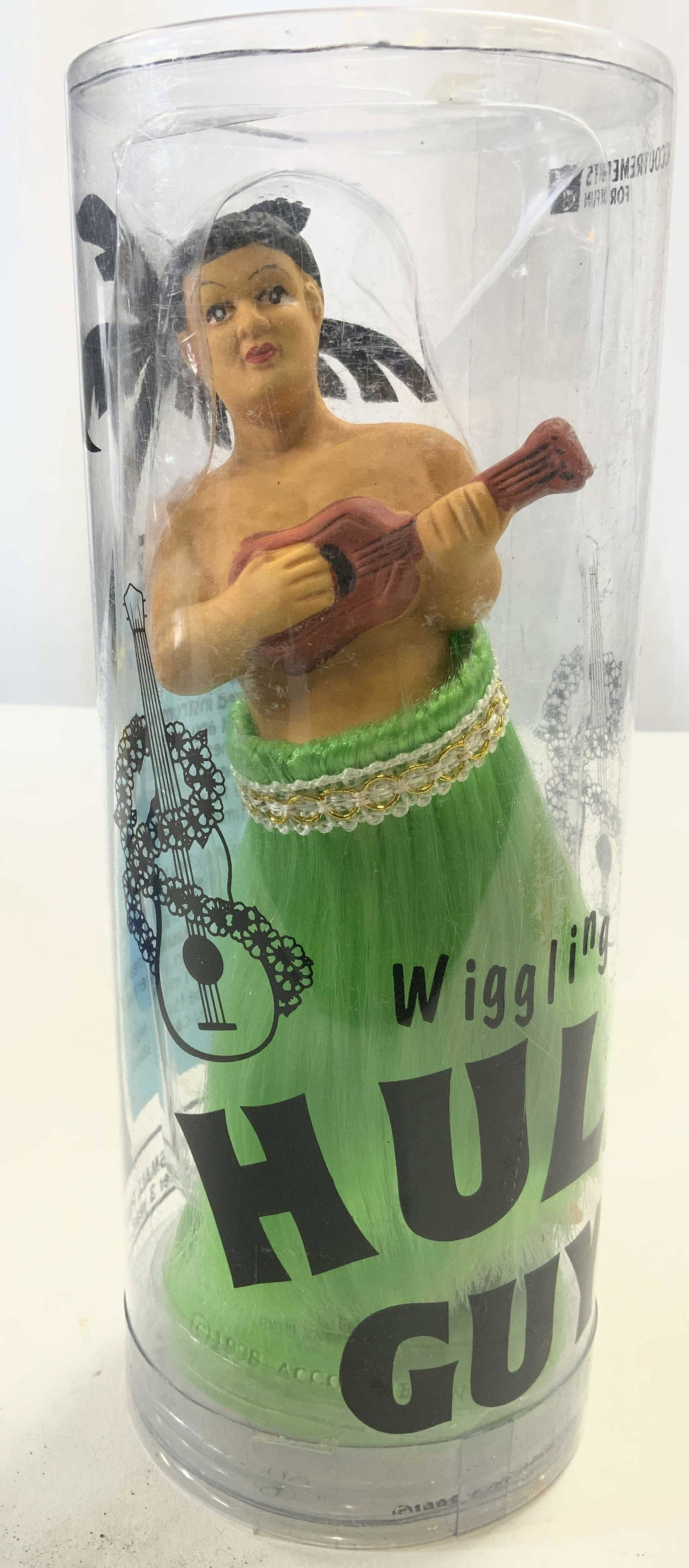 ACCOUTREMENTS Wiggling Hula Guy NIB: Box reads ACCOUTREMENTS WIGGLING HULA GUY. Piece shows male figure with hula skirt & ukulele. Base reads ALOHA. Box measures approx 7.75 inches tall 3 inches wide. Accoutrements, accoutrements hula gu