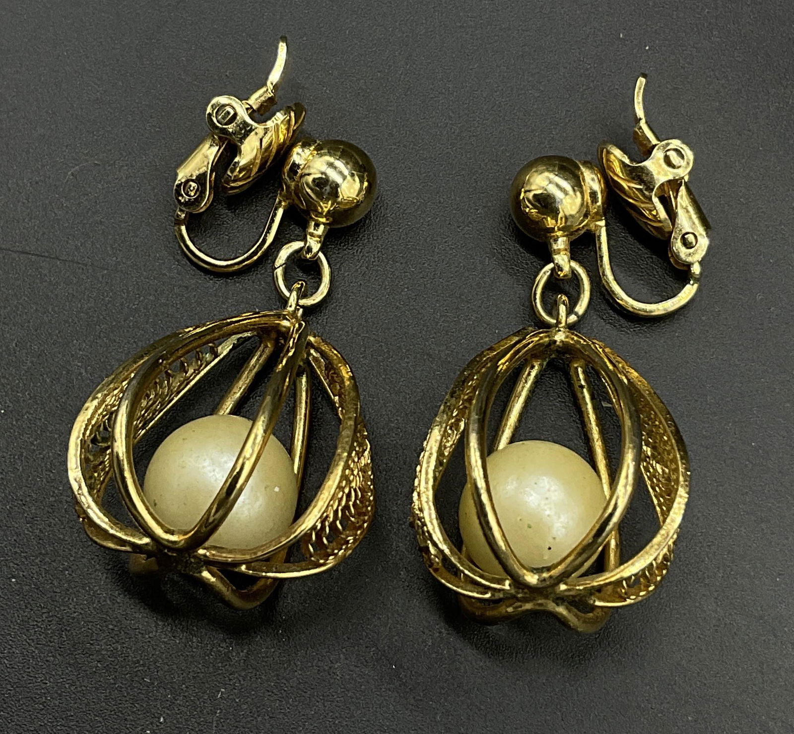 TRIFARI Clip On Caged Pearlescent Earrings: Sgnd TRIFARI Clip On Caged Pearlescent Earrings. Caged pearlescent piece in gold toned metal. Earrings signed TRIFARI on back of clips. Measures approx 1 inch. Earrings, pearlescent earrings, TRIFARI