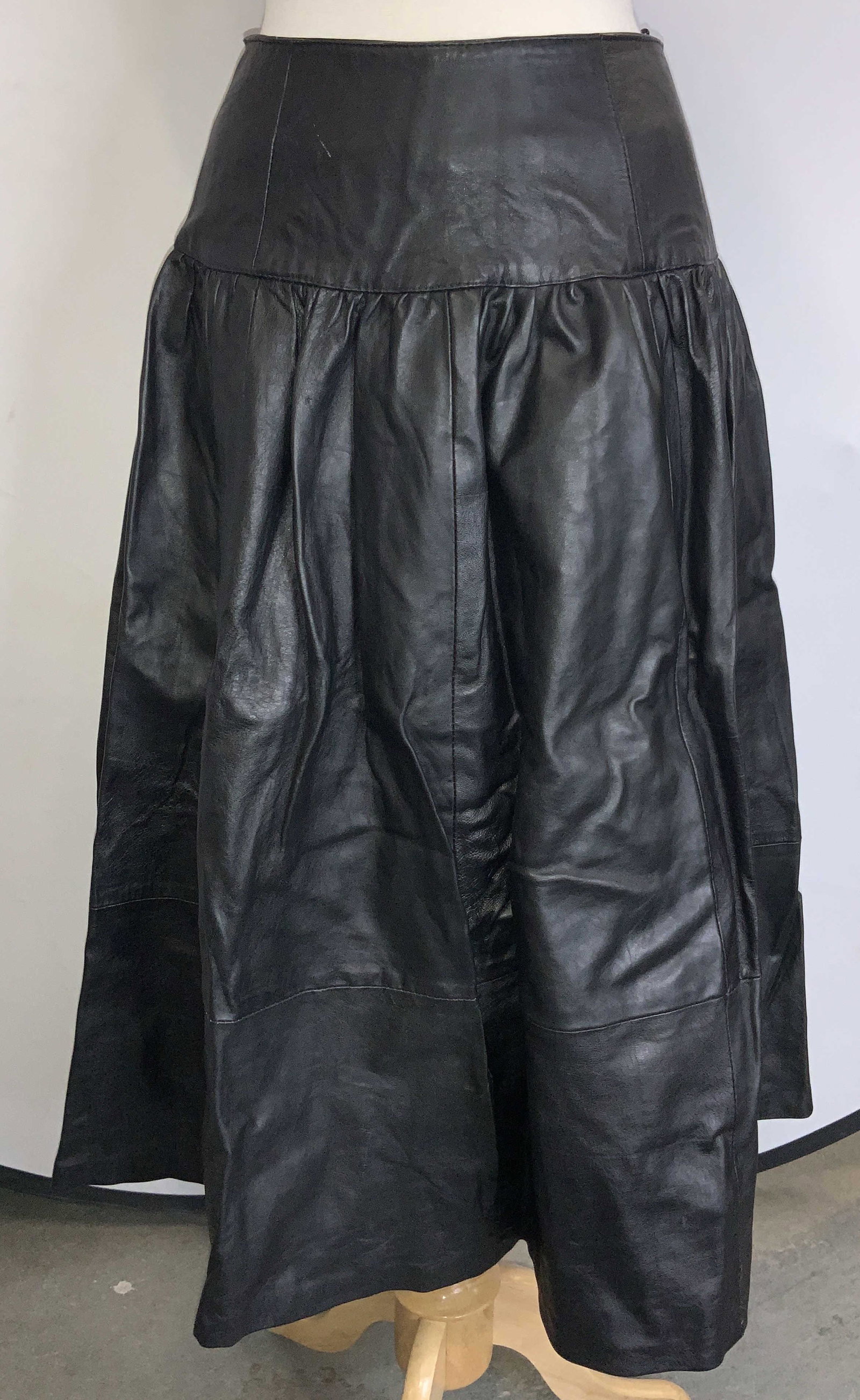 Size Large Genuine Black Leather Skirt: Black shirt, approximately 31 inches long. Material tag reads 100% Genuine leather, size Large. Waist measures 28 inches around. Buttons are marked Waldes. Minor blemishes to leather. Genuine leather 