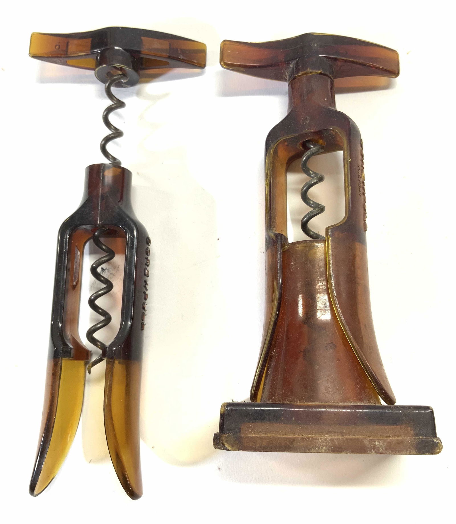 Lot 2 Vintage Bakelite Screw Pulls: Lot includes 2 screw pulls. Each are amber toned and appear to be Bakelite. Sides of each piece read SCREWPULL. Largest screw pull measures approx 6.25 inches tall 3 inches wide. Screw pulls, wine cor