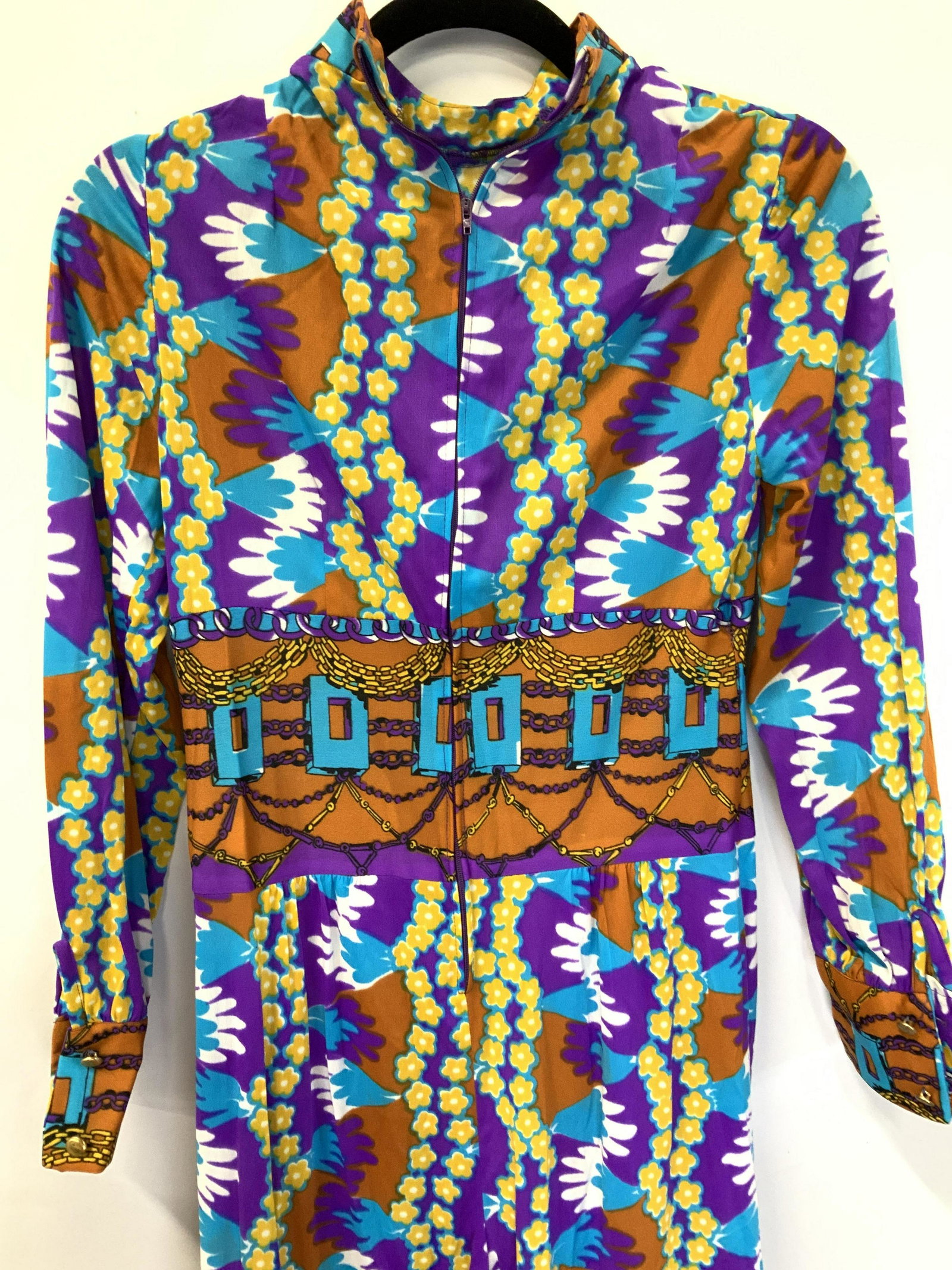 Mid Century Pop Boot Leg Jumpsuit: Zipper Jumpsuit, flared legs, dynamic pattern and colors of purple, turquoise, brown and yellow flowers. Buttoned cuff. Fabric is a semi sheer polyester. Union made in the USA. WAIST 26-27 in. Total l
