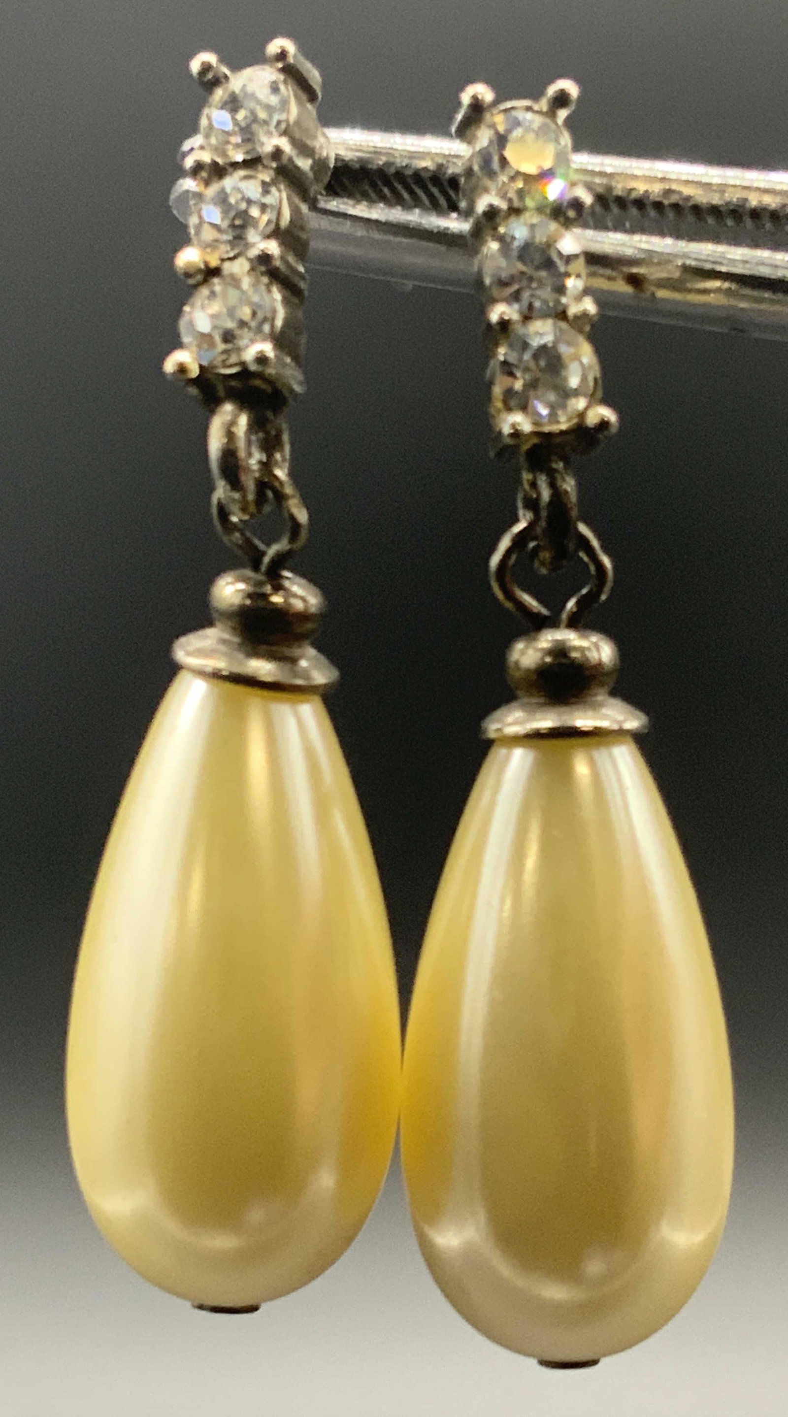 Vintage Pearlescent Teardrop Bead Drop Earrings: Vintage teardrop pearlescent bead drop earrings. Colorless faceted crystals along a bar affixed to the pearlescent bead via bail. Backings for pierced ears. Measures approx 1.75L x .5W in. Some wear c