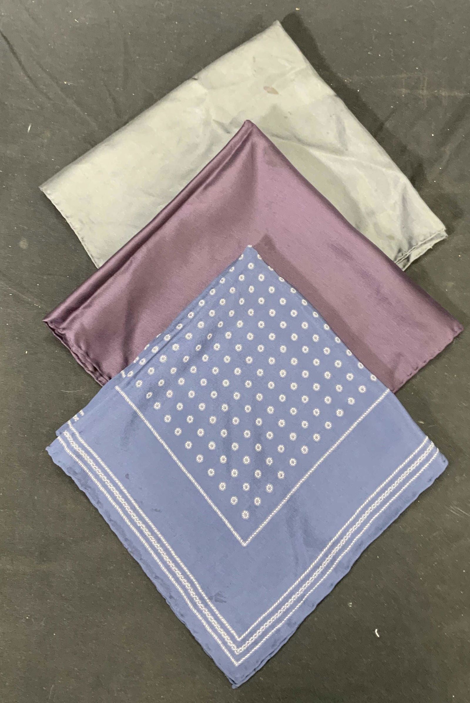 Lot 3 Blue, Purple, & Grey Silk Pocket Squares: 3 silk pocket squares with hand rolled hems in hues of purple, blue, and grey. Sizes vary, largest approx. 18 x 18.5 inches. All pocket squares have some blemishes to fabric. Pocket square, mens pocke