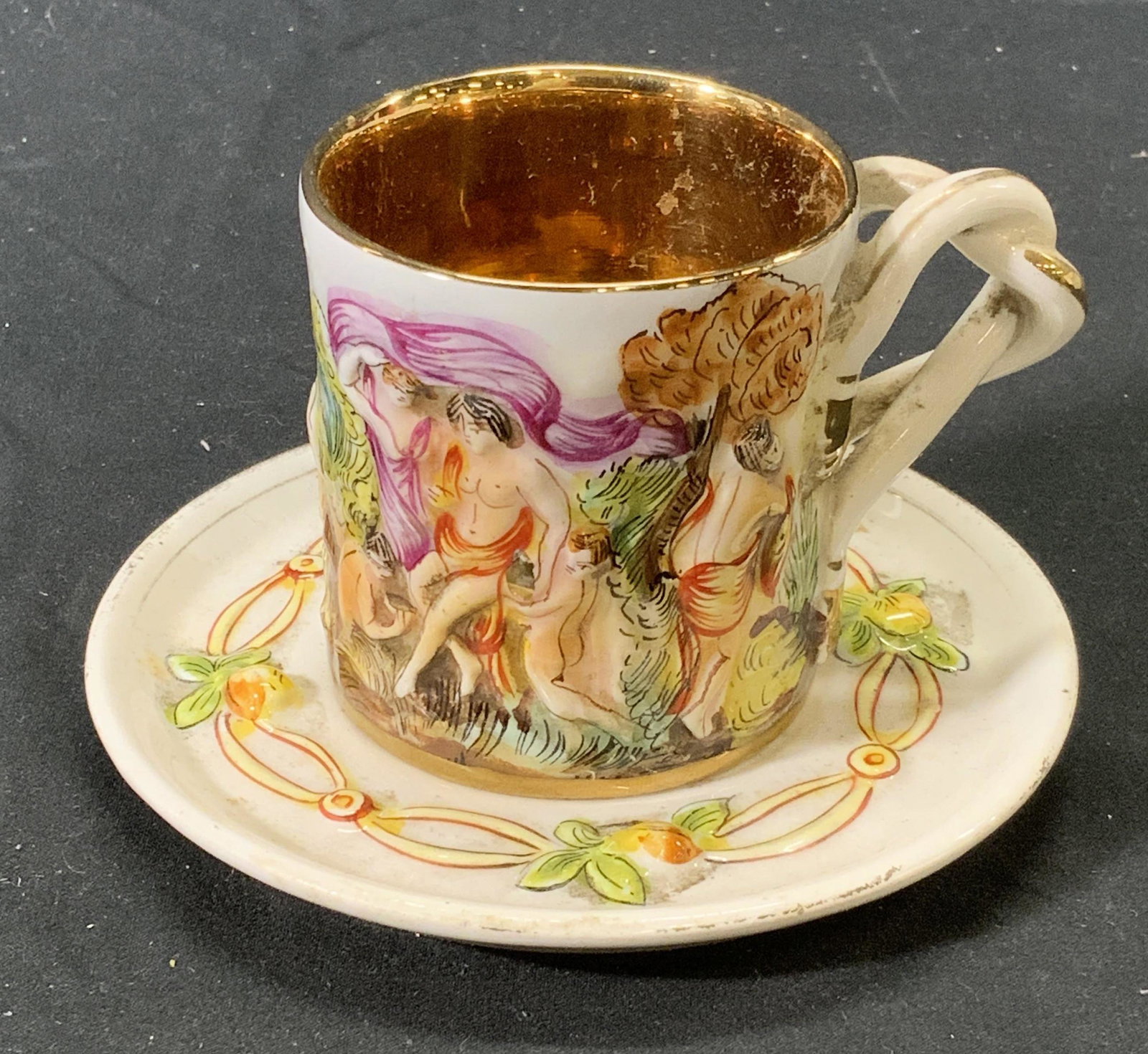 Vintage CAPODIMONTE Porcelain Demitasse & Saucer: Pair on vintage Capodimonte porcelain demitasse cup and saucer. Cup displays figural motif in surface relief and gilt interior. Saucer displays floral motif in surface relief. Cup measures approx. 2.2