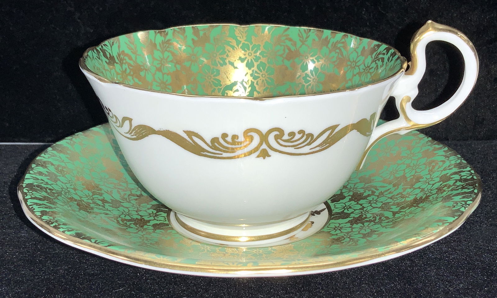 AYNSLEY Fine Bone China Tea Cup & Saucer, England: Hand painted fine bone China , white porcelain with green overlay and detailed floral gilt pattern. Made in England, Hallmarked Aynsley England c 960. Saucer 5.5 in diameter , cup 2.25 in ht. Chinawar