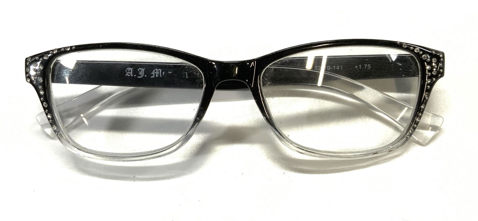 AJ MORGAN Black Crystal Reading Glasses: AJ MORGAN black reading glasses with crystal detail to frame. +1.75 magnification. Designer label to interior arm. Surface consistent with exposure. reading glasses, eye glasses, fashion,fashion acces