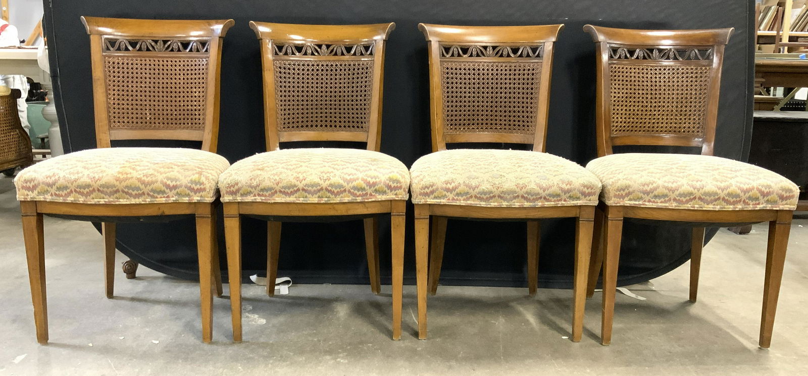 Vintage Caned Wooden Upholstered Side Chairs: Side chairs are vintage. Each piece has caned backrests. Chairs each have upholstered seats with double welting at edges. Upper areas of backrests have carved vine & leaf detail. Chairs each measure a