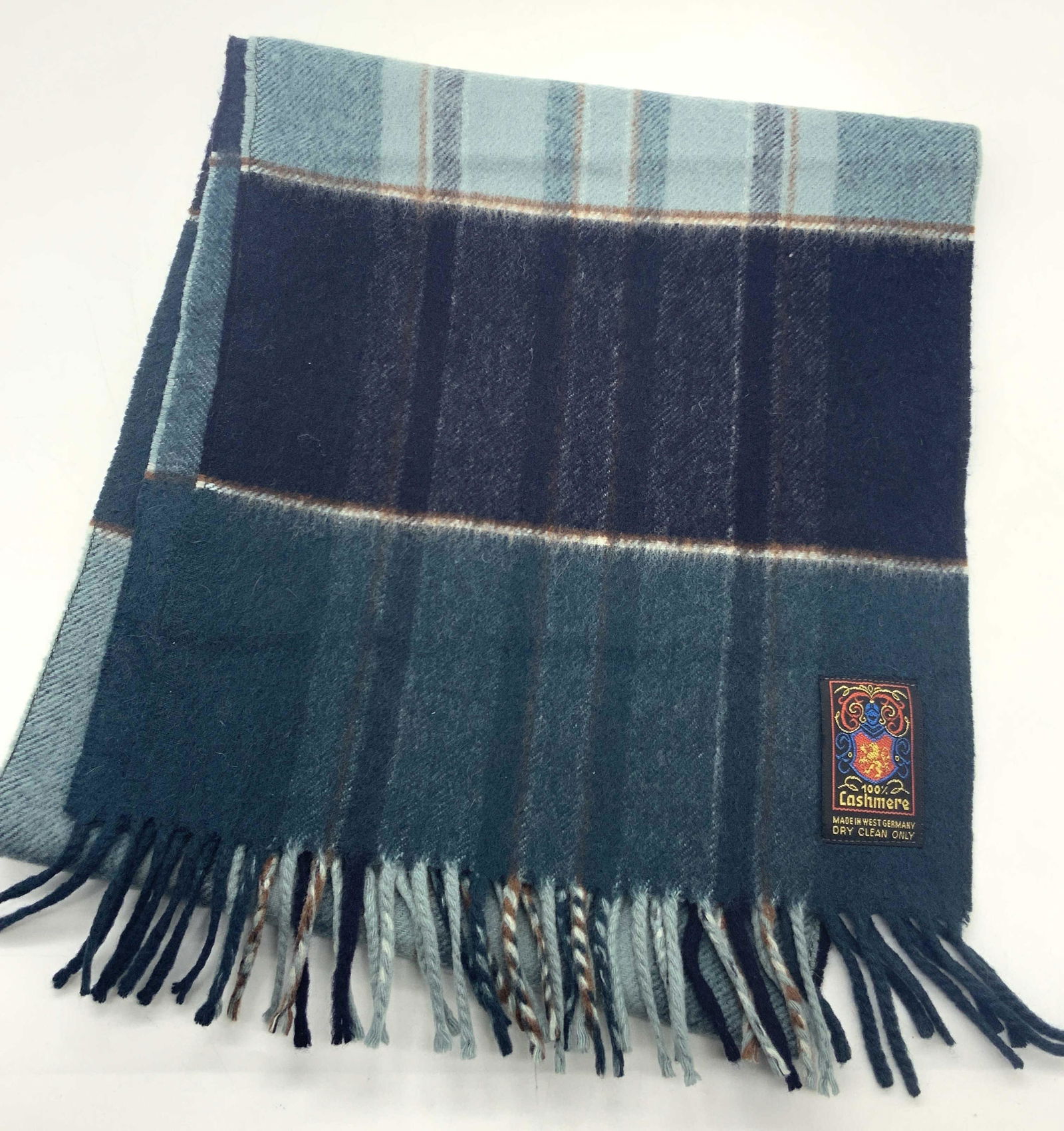 100% Cashmere Plaid Scarf, West Germany: Marked on material tag 100% Cashmere, West Germany with embroidered shield in blue with a gold lion in the center. Scarf has various tones of teal with brown accent lines in plaid pattern. Approximate