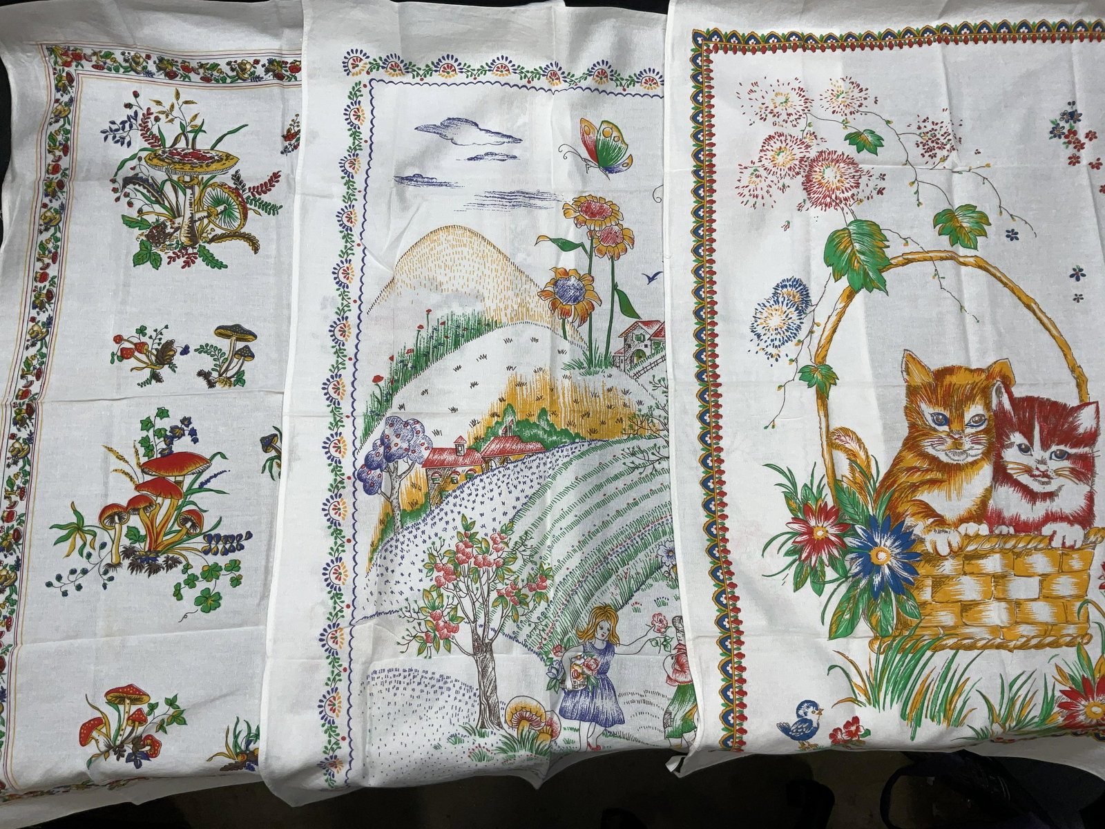Lot 3 Cotton Kitchen Linens: Lot 3 Cotton Kitchen Linens. Material Label reads 100% cotton. Minimal stain present to pieces. Detail to towels include mushrooms, kittens in a basket and a landscape scene with 2 figures. Tea towel,