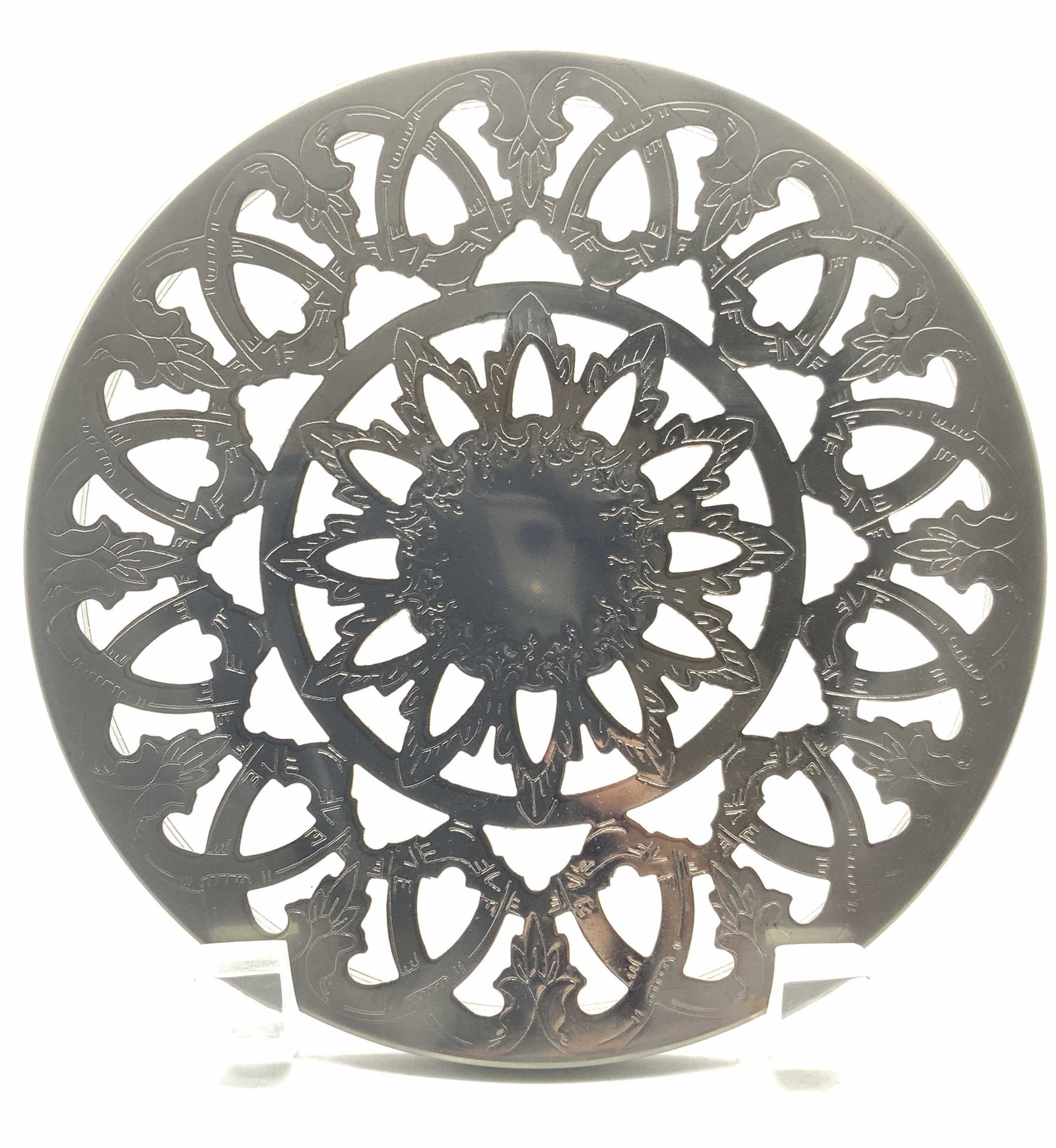 Vintage Ornate Silver Plate Trivet: Vintage ornate trivet, possibly silver plate, with ornate geometric cut outs and etchings throughout. Approximately 6 inch diameter. Evident discoloration to center. Ornate trivet, vintage trivet, tri
