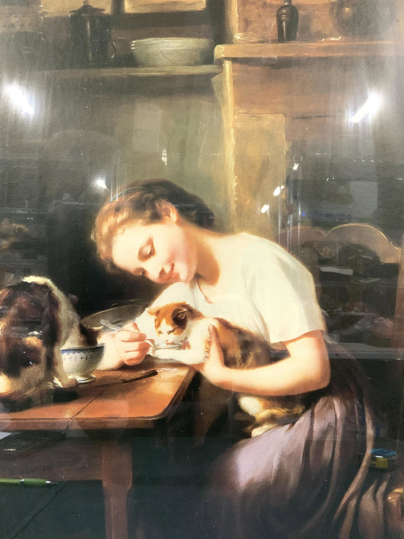 FRITZ BULER Little Girl With Cats Lithograph: A framed Lithograph depicting a young girl at a table holding a cat in her arms as it licks milk out of spoon and another cat sitting on the table drinking out of bowl. Original painting done by Fritz