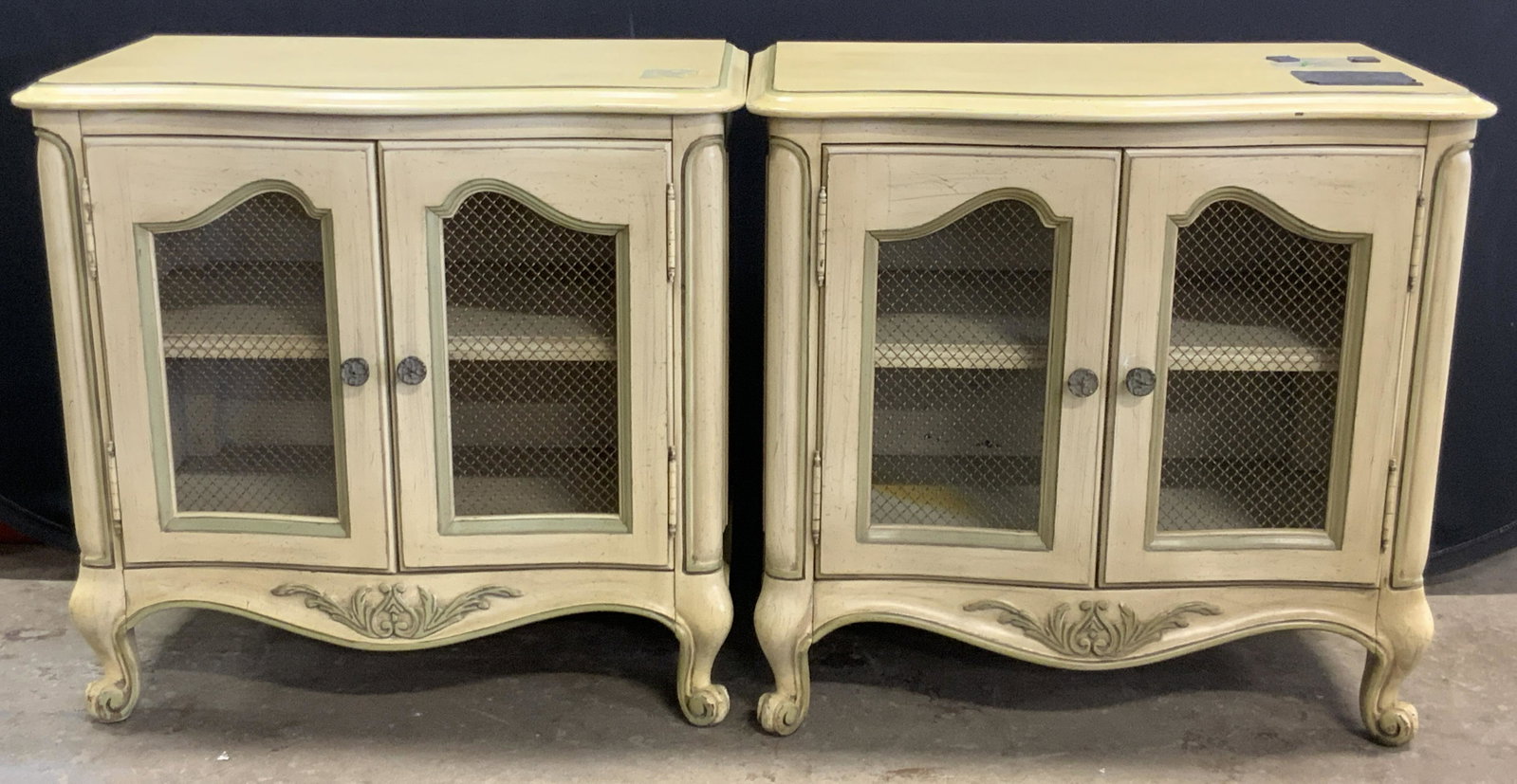 Pair Vintage French Country Wooden Nightstands: A pair of vintage French Country style nightstands. Crafted from wood. Yellow and green hues. Metal drawer pulls to the cabinets. Mesh overlay to the cabinets. Curled feet. Sticker residue / stickers 