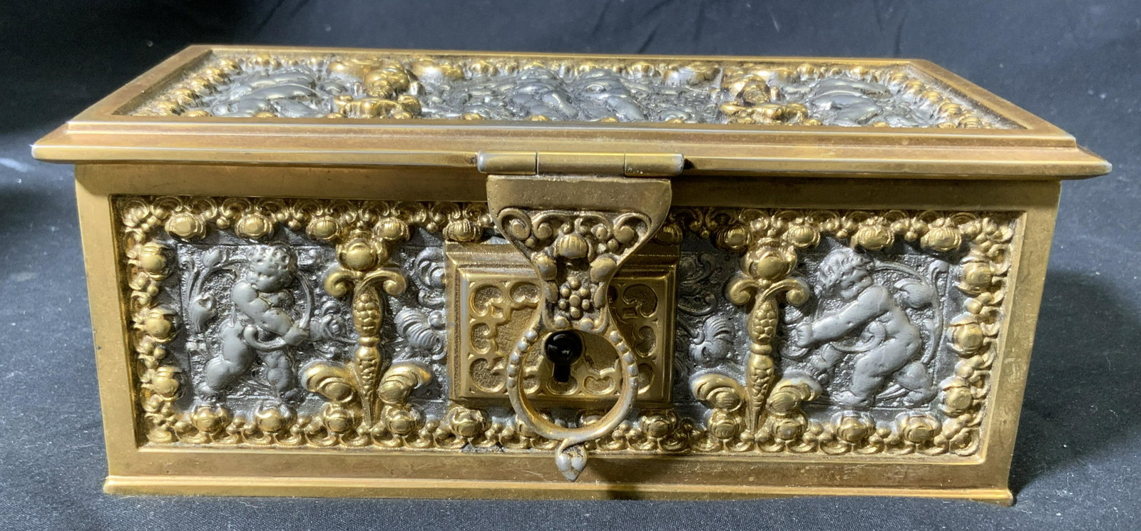Vintage Heavy Gold Plated Jewelry Lock Box: Vintage gold plated and silver tone jewelry/lock box. Does not include key. Figural cherub motif debossed to outer. Interior blue felt lined. Surface wear consistent with exposure. Measures approx. 6.