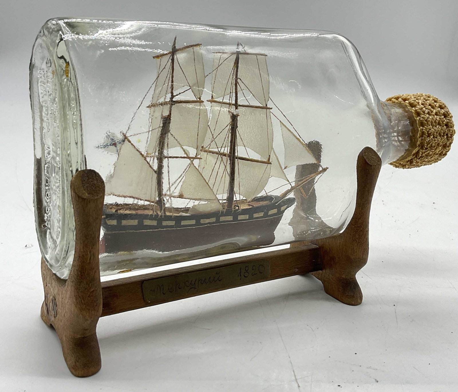 Ship In Glass Bottle, W Signed Plaque: Ship In Glass Bottle, W Signed Plaque. Plaque is not Fully legible, name is followed by a date of 1820. No visible wear to piece. Glass attached to stand. Measures approx 7 x 4.5 inches. Ship in bottl