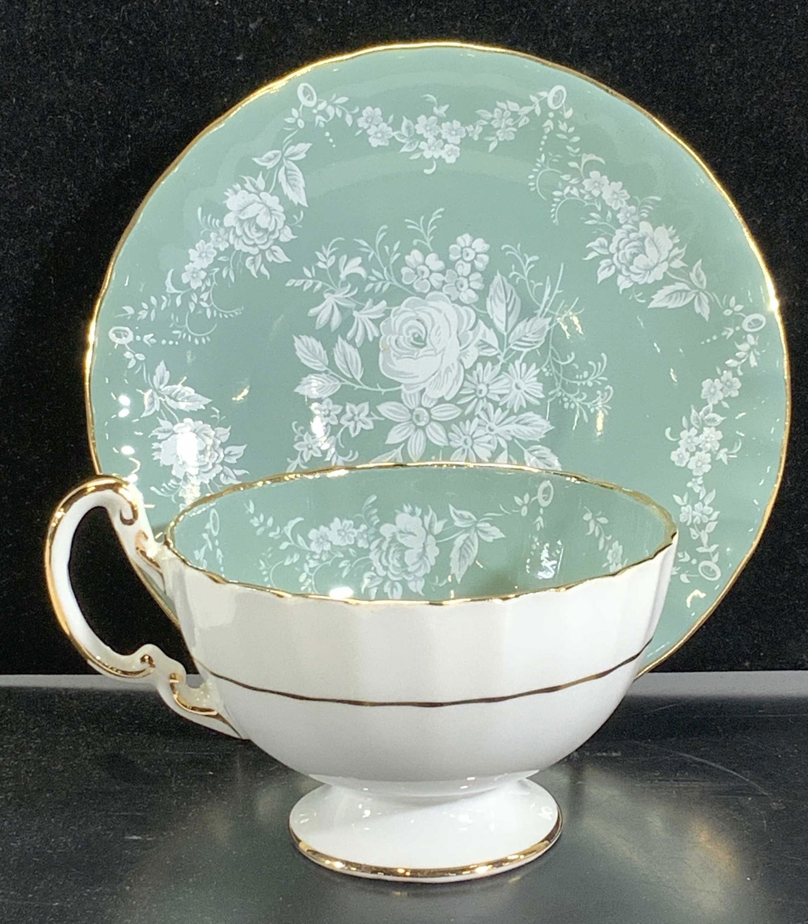 Aynsley Footed Porcelain Tea cup & Saucer, England: Hand painted tea cup and saucer, white underside with mint green and white painted roses, gilt rims. Footed cup measures 2.25 in ht, 3.5 in wide ( cup only not handle) , saucer measures 5.5 in. Hallma