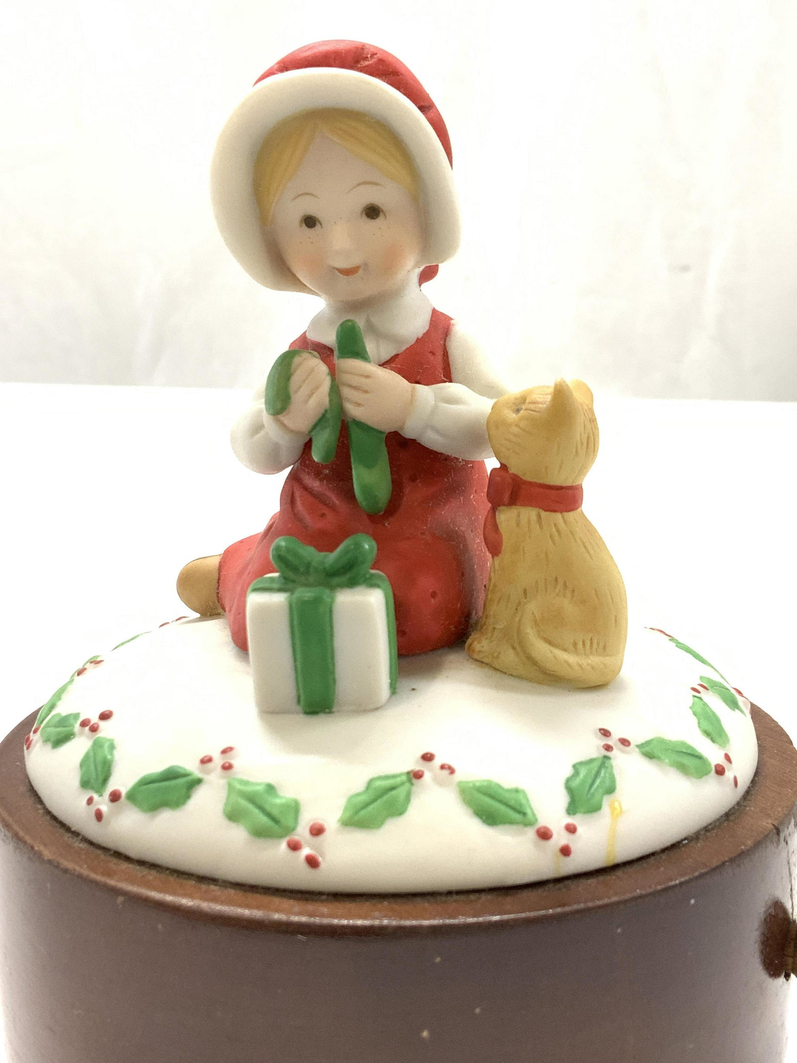 Porcelain & Wood Music Box, My Favorite Things: Hand painted Girl with her cat wrapping a Christmas Gift on wood base. Pull lever and wind music box to play My Favorite Things from The Sound of Music. Measures 5 x 4.5 in. Comes in a storage box. 3 
