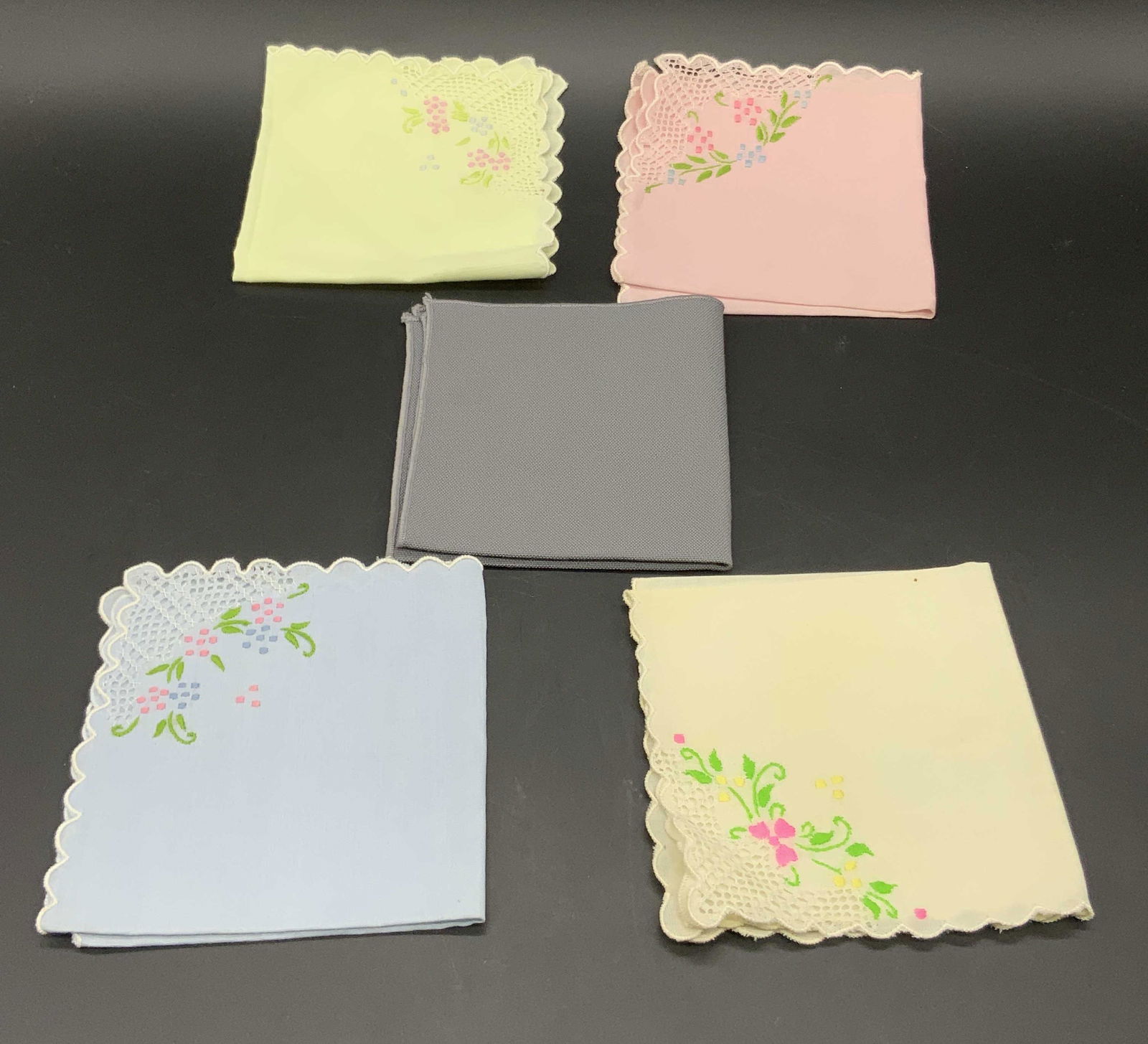 Lot 5 Embroidered Scalloped Fabric Napkins & More: Four embroidered scalloped rimmed fabric napkins. Pink, blue, and yellow hues with pink, blue, and green embroidery. Pierced fabric accents alongside embroidery. One gray hued fabric napkin accompanie