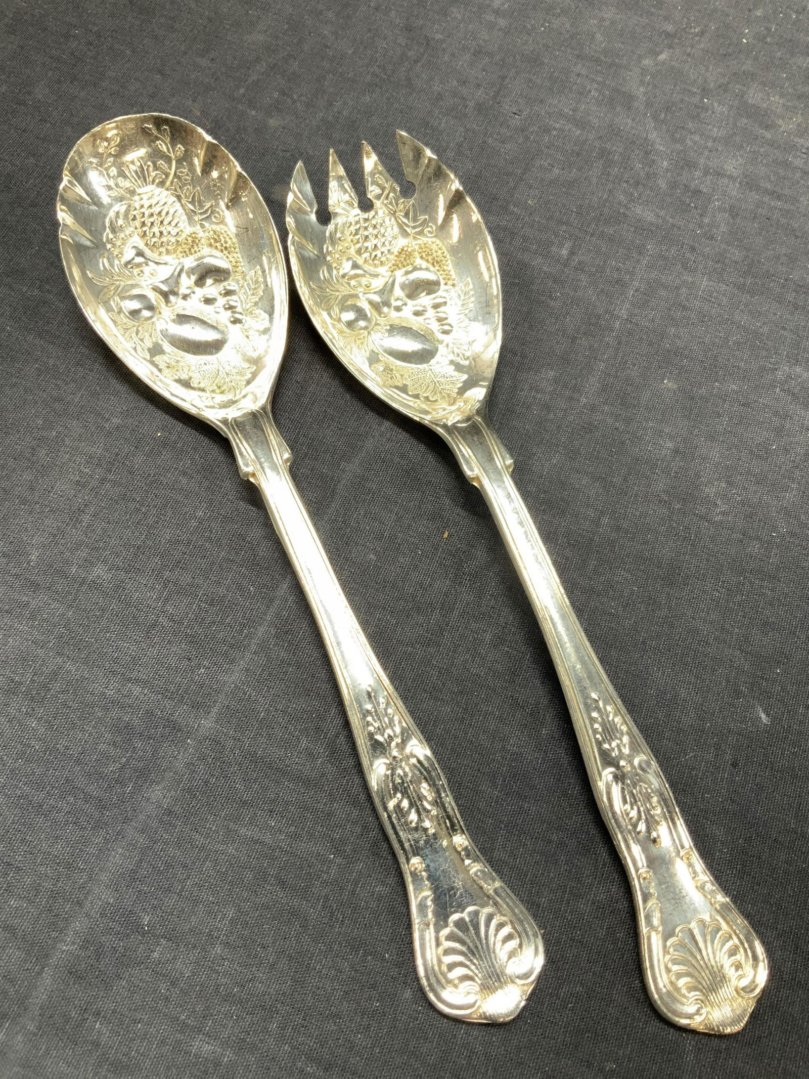 Ornate Embossed Steel Serving Utensils, Italy: Set of ornate steel serving utensils 1 spoon and spork, embossed with fruit and floral motifs on inside bowl, marked Italy on undersides. Approximately 9 inches long. Minor surface wear. Steel utensil