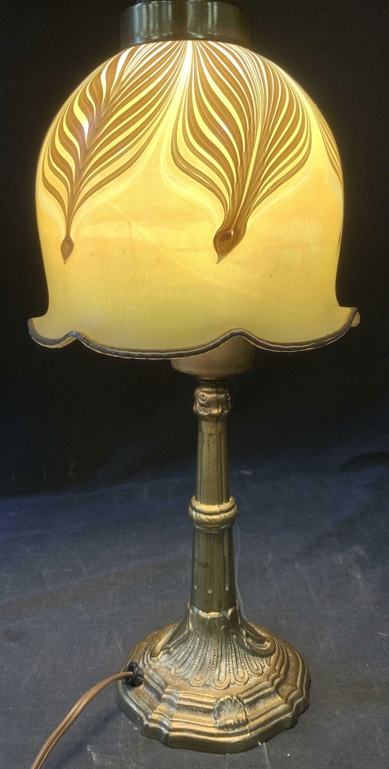 Iridescent Favrile Style Pulled Feather Glass Lamp: Vintage Early 20th century Favrile pulled feather style satin glass lamp with brass column. Art nouveau in style , chased brass depicting loops and shells .on / off switch on on cord. Brass finial. Ar