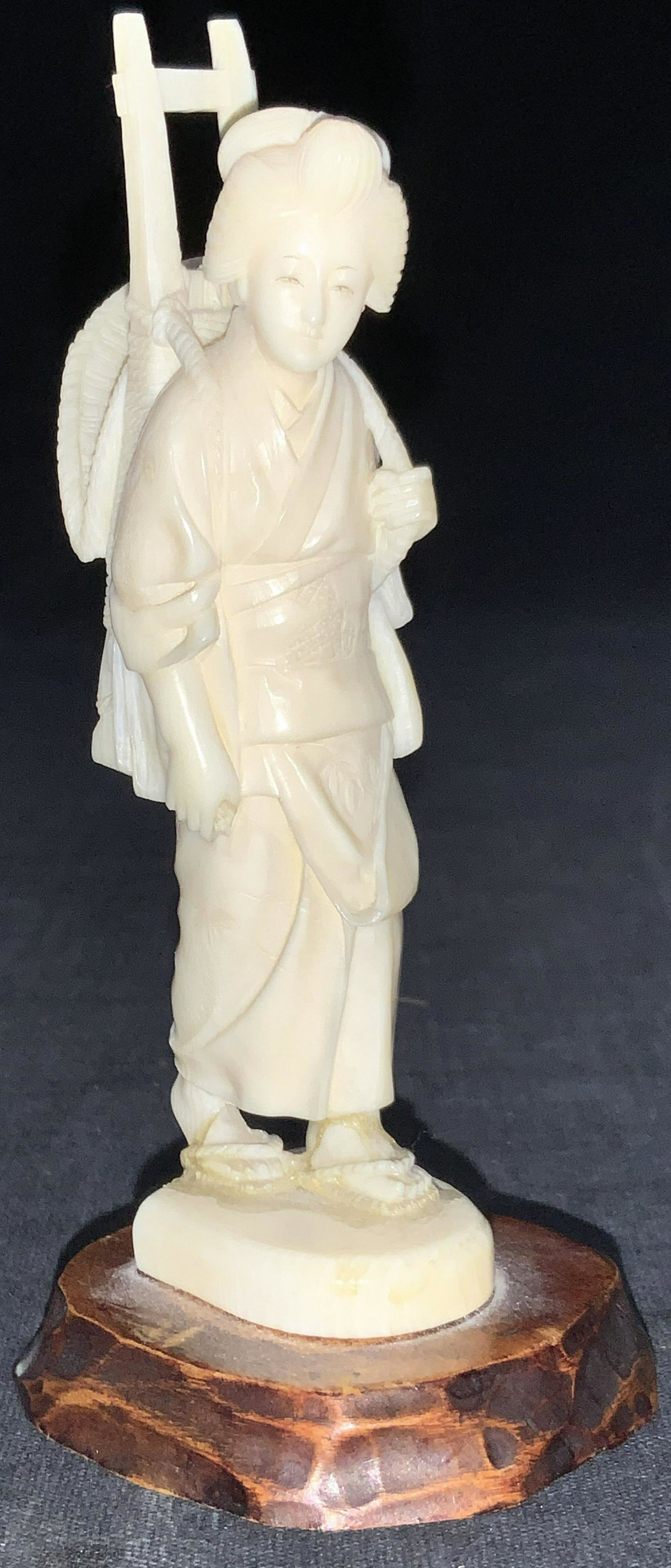 Japanese Woman Resin Figural: Resin Figural depicting a waking Japanese woman with hair in an updo holding a rack with a straw hat attached. Figure is intricately carved with floral patterns in the kimono and the Individual strand