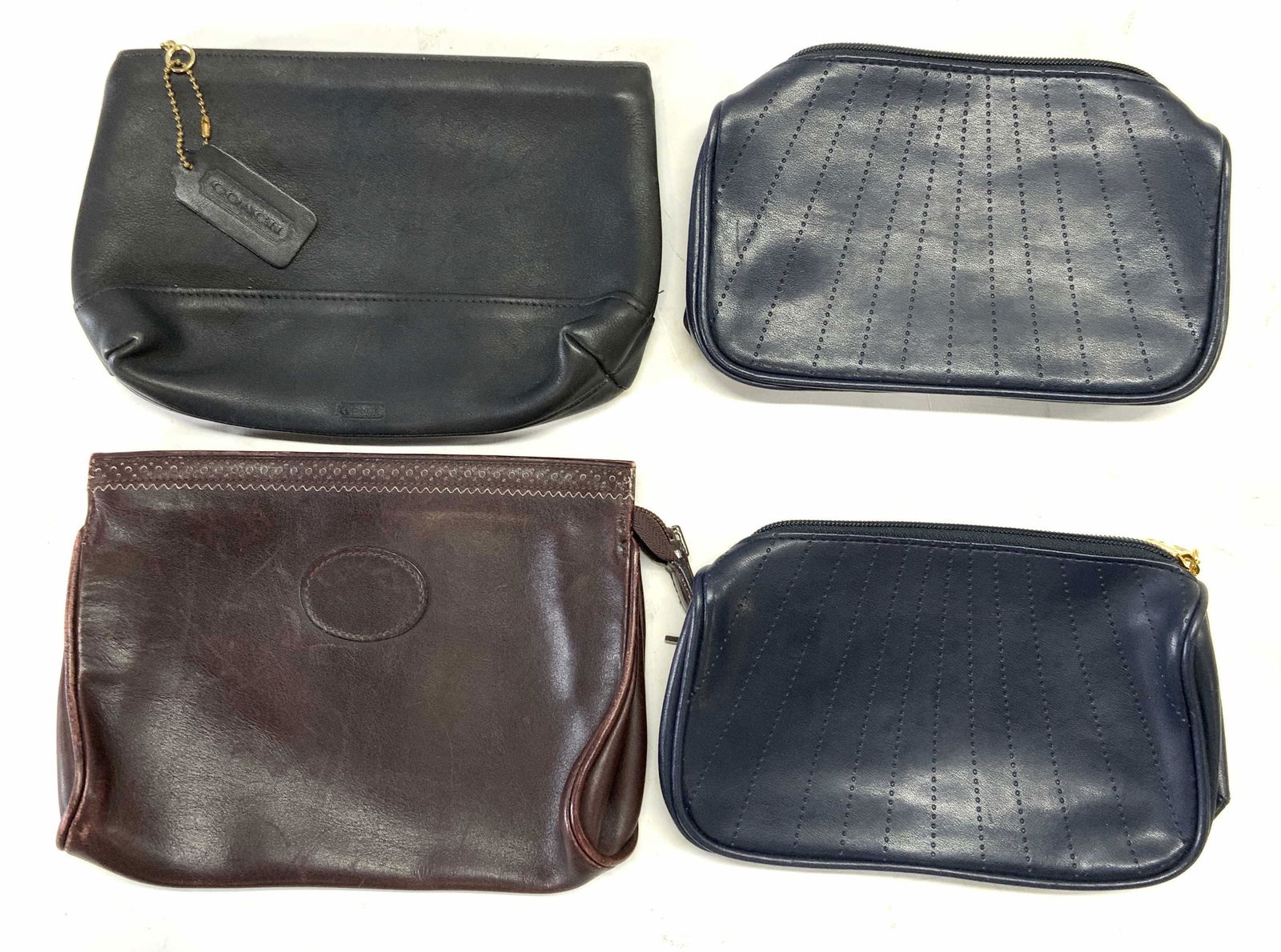 Lot 4 COACH & More Designer Zippered Pouches: 1 black leather Coach zippered pouch. Marked Coach to leather tag on exterior. Measures approx. 9 x 6 inches. 1 burgundy leather Cross zippered pouch. Marked Cross Italy to interior. Measures approx.