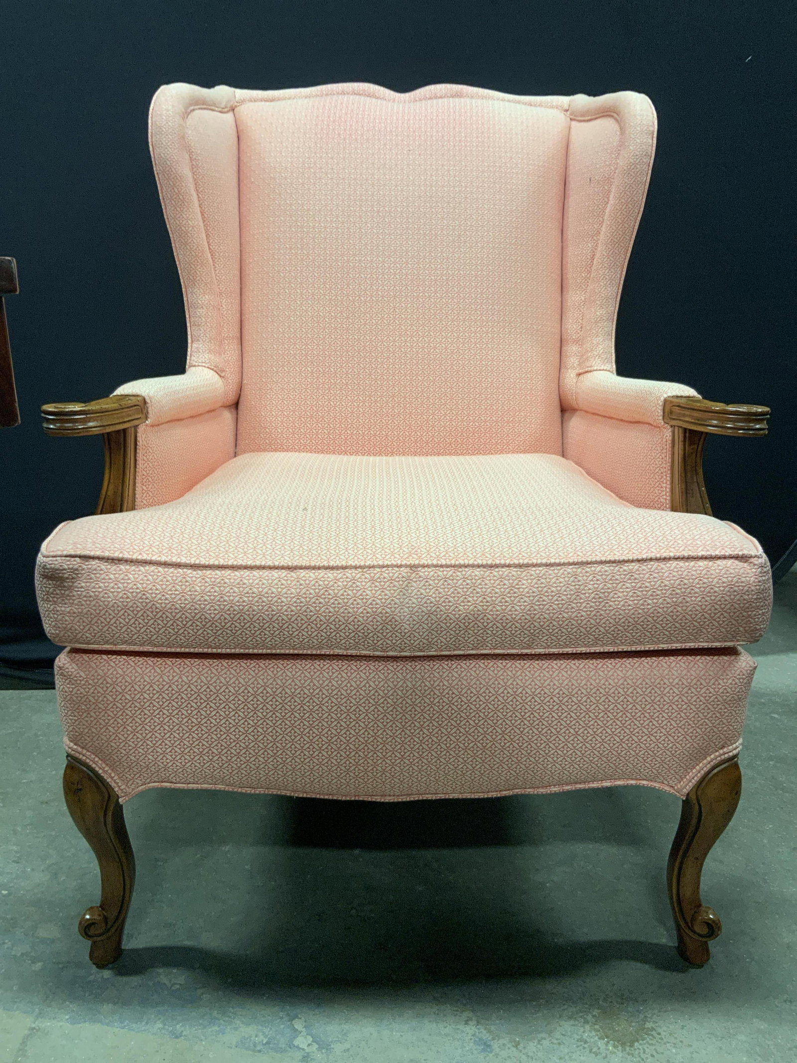 Vintage Upholstered Wingback Armchair Pink: Armchair is vintage. Piece has pink toned geometrically patterned upholstery. Some edges of upholstery have double welting. Chair has carved wooden legs. Measures approx 40 inches tall 30 inches wide 