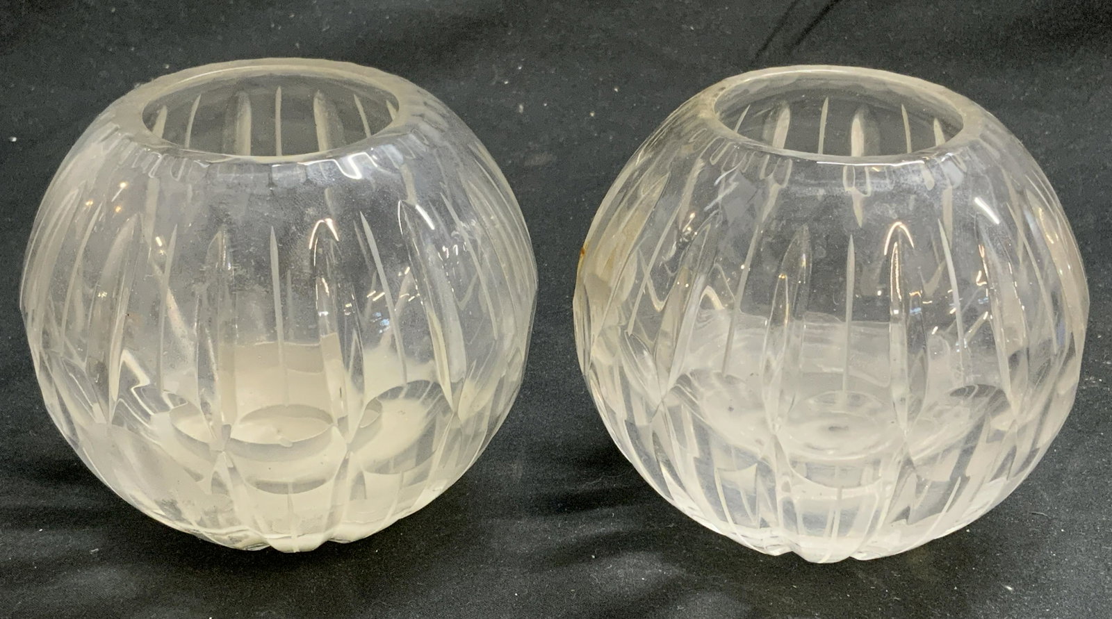 Pair Round Cut Glass Vessels: Pair of round cut glass vessels. May be used as votive candle holders, decorative vessel, or Bud vase. Measure approx. 4 inches diameter and 3.5 inches tall each. Crack to one vessel. Need cleaning. C
