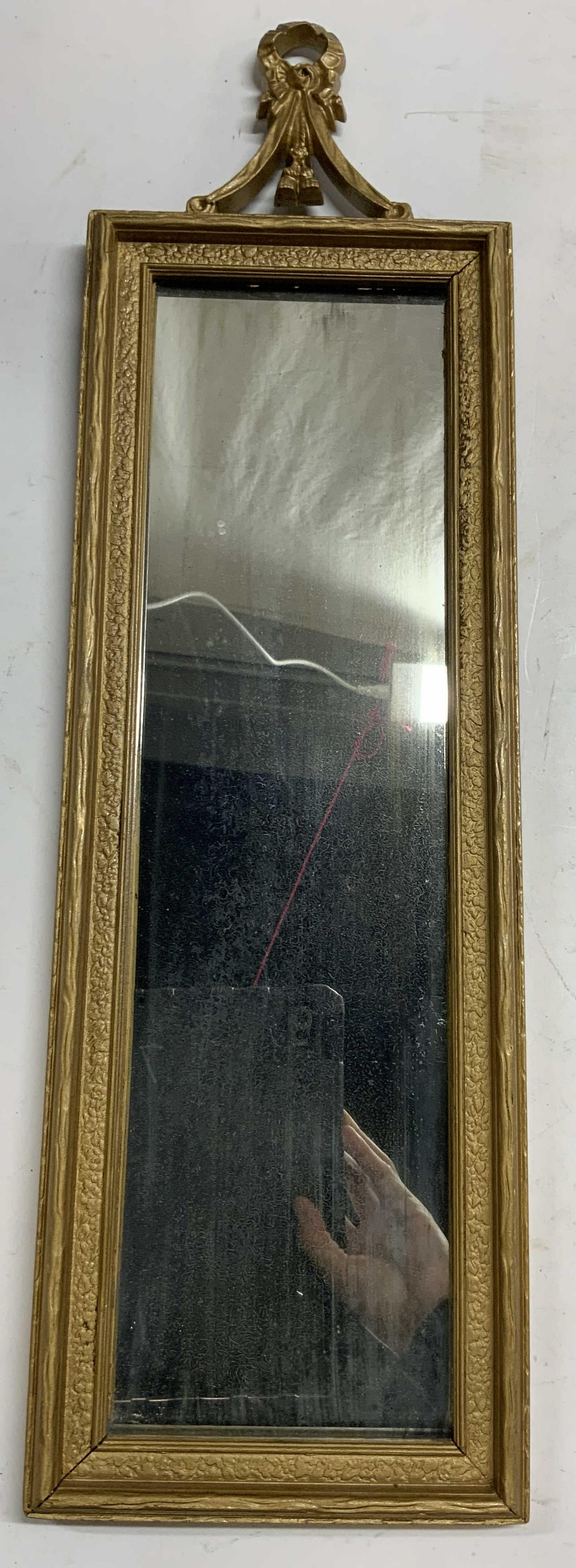JS MFG CO Vntg Ornate Giltwood Wall Mirror: Backside reads JS MFG CO. Mirror is vintage. Piece has gold toned Giltwood frame. Top of frame has ornate detail. Piece measures approx 22.5 inches tall 7 inches wide. Mirror, wall mirror, Giltwood mi