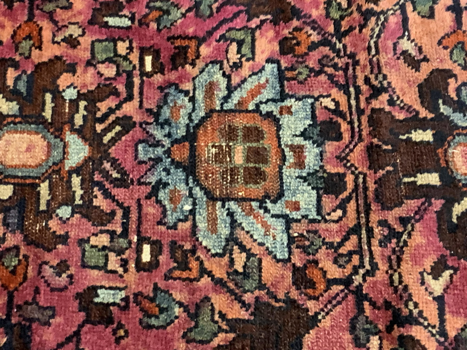 Vintage Persian Area Rug: A vintage Persian area rug. Deep rust, magenta, and earth tones alongside pops of blue. Piece appears to be handmade and crafted from wool. Measures approx 45L x 30W in. Some surface wear consistent w