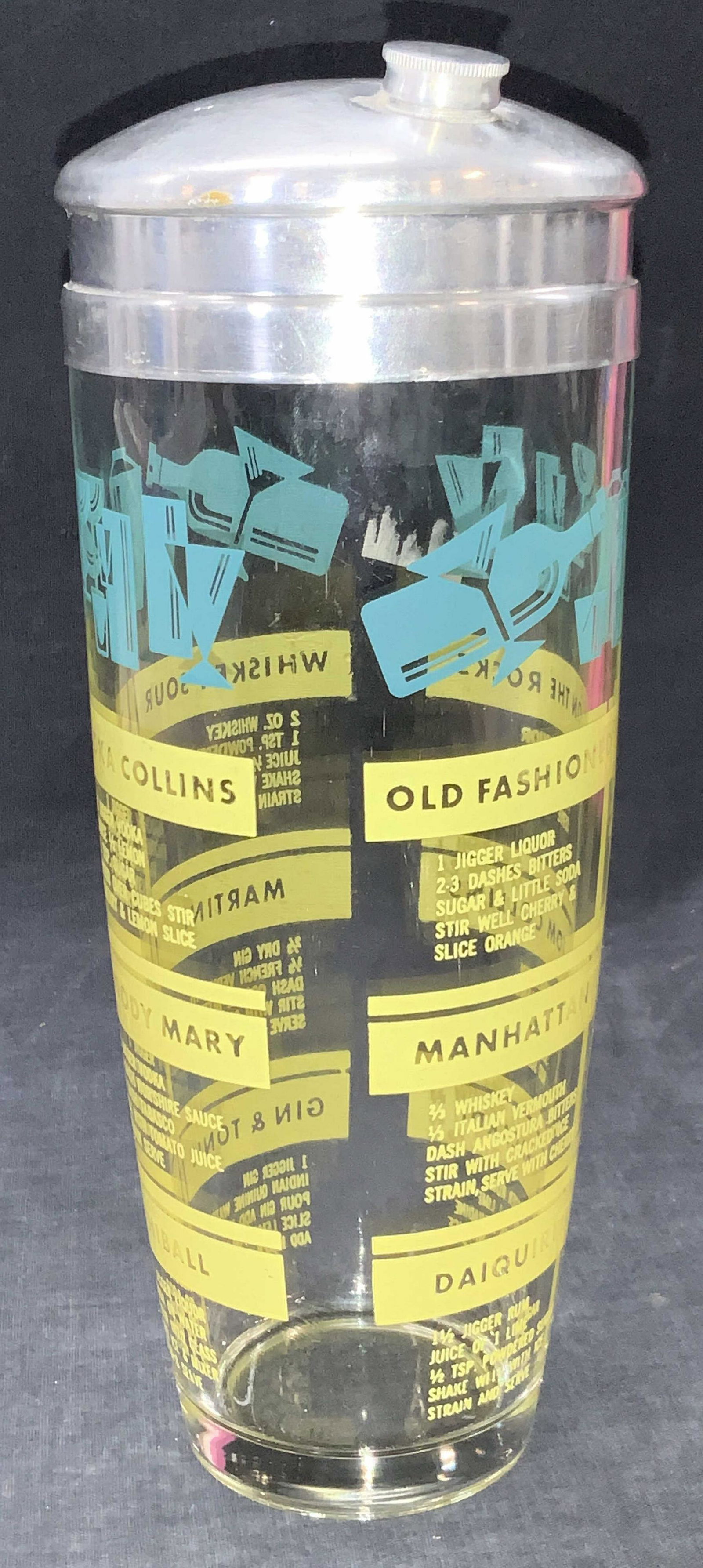 Vintage Glass Drink Mixer: Vintage glass drink mixer with white metal lid. Glass tumbler has decals on exterior with drink recipes and motifs of drink glasses and tumblers in teal. Approximately 9.75 inches tall. Evident wearin