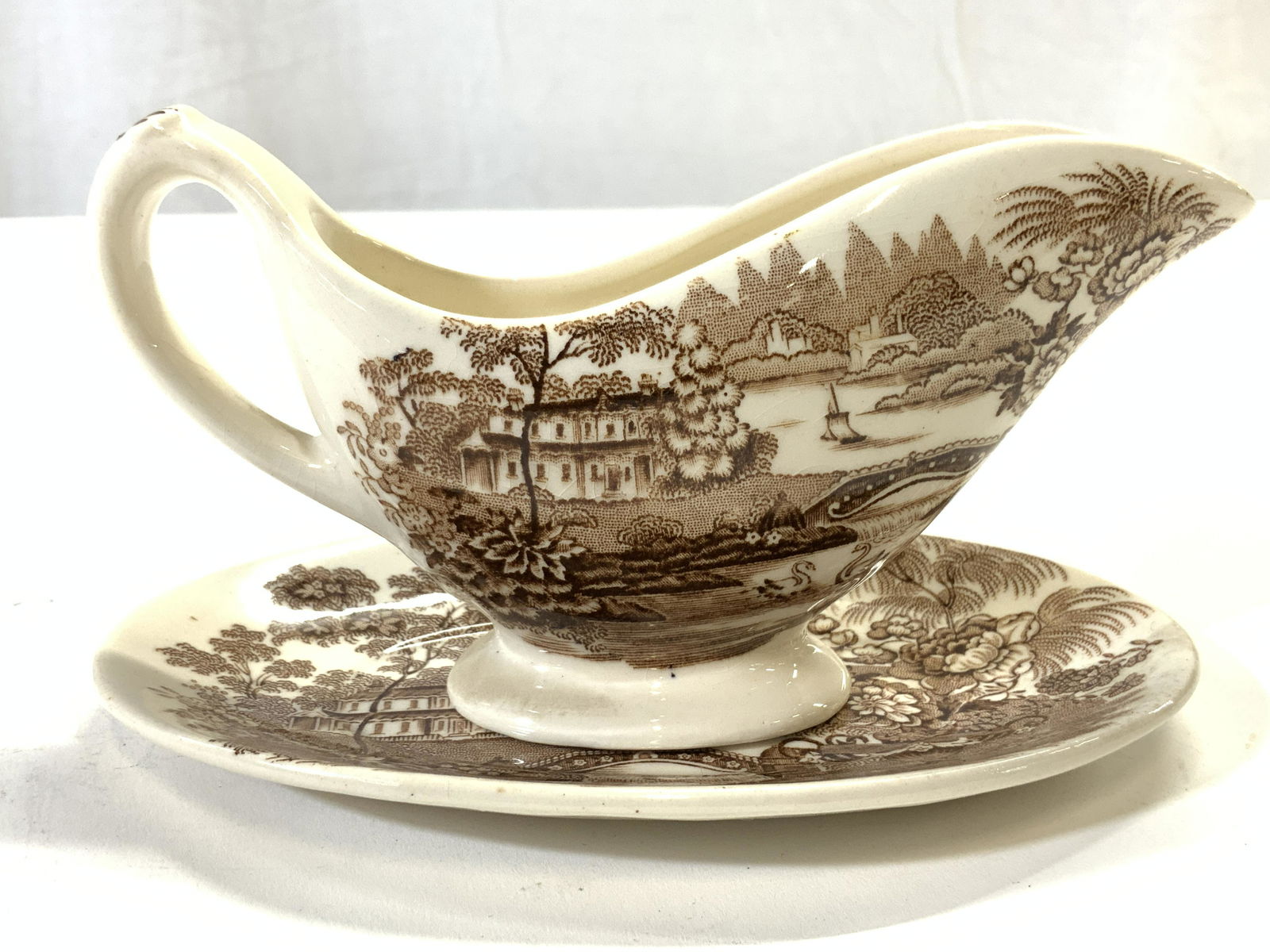 Set 2 STAFFORDSHIRE Gravy Pourer & Saucer: Lot includes 1 gravy pourer & 1 saucer. Each piece is marked ROYAL STAFFORDSHIRE DINNERWARE BY CLARICE CLIFF TONQUIN on underside. Each piece is cream with brown toned landscape detail. Saucer measure