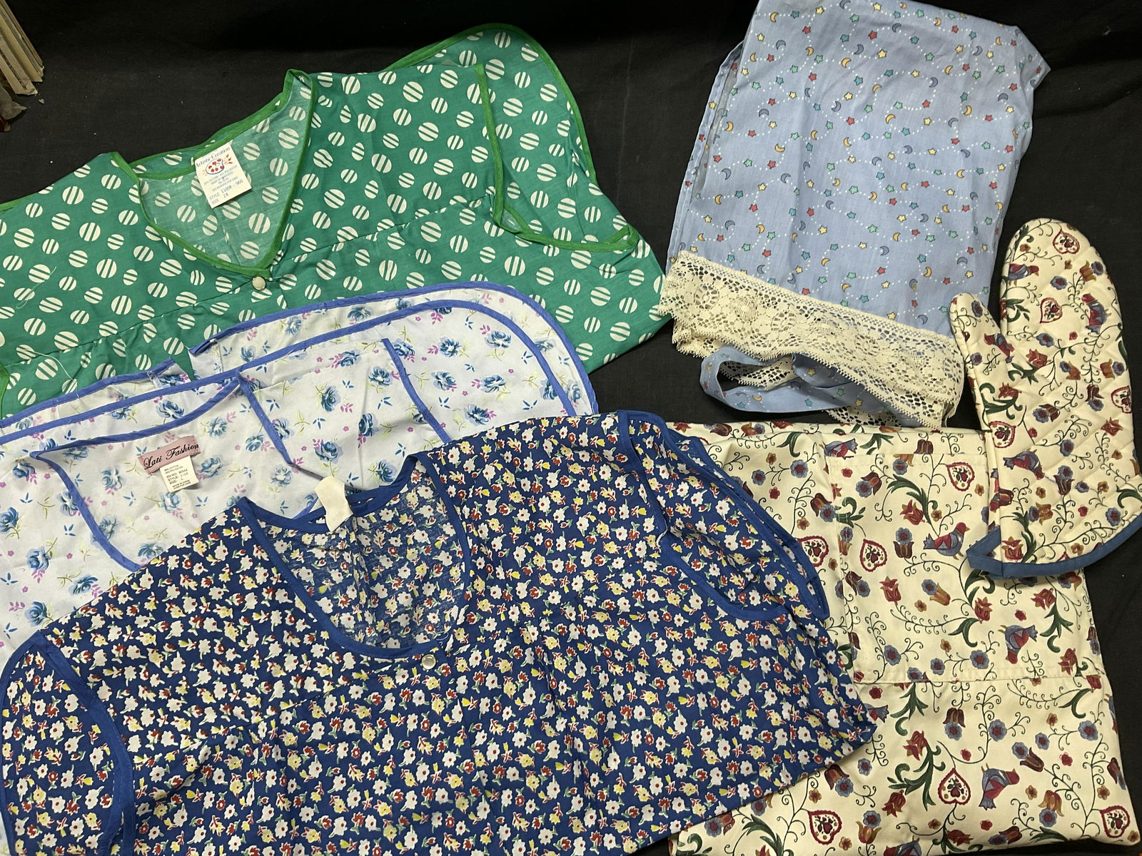 Lot 6 Art/ Cooking Aprons & Oven Mitt: Lot 6 Art/ Cooking Aprons & Oven Mitt. Aprons sized and have material labels to them (see photos) largest is 2XL. Some staining to some pieces. (See photos). Some buttons are not fully attached, need