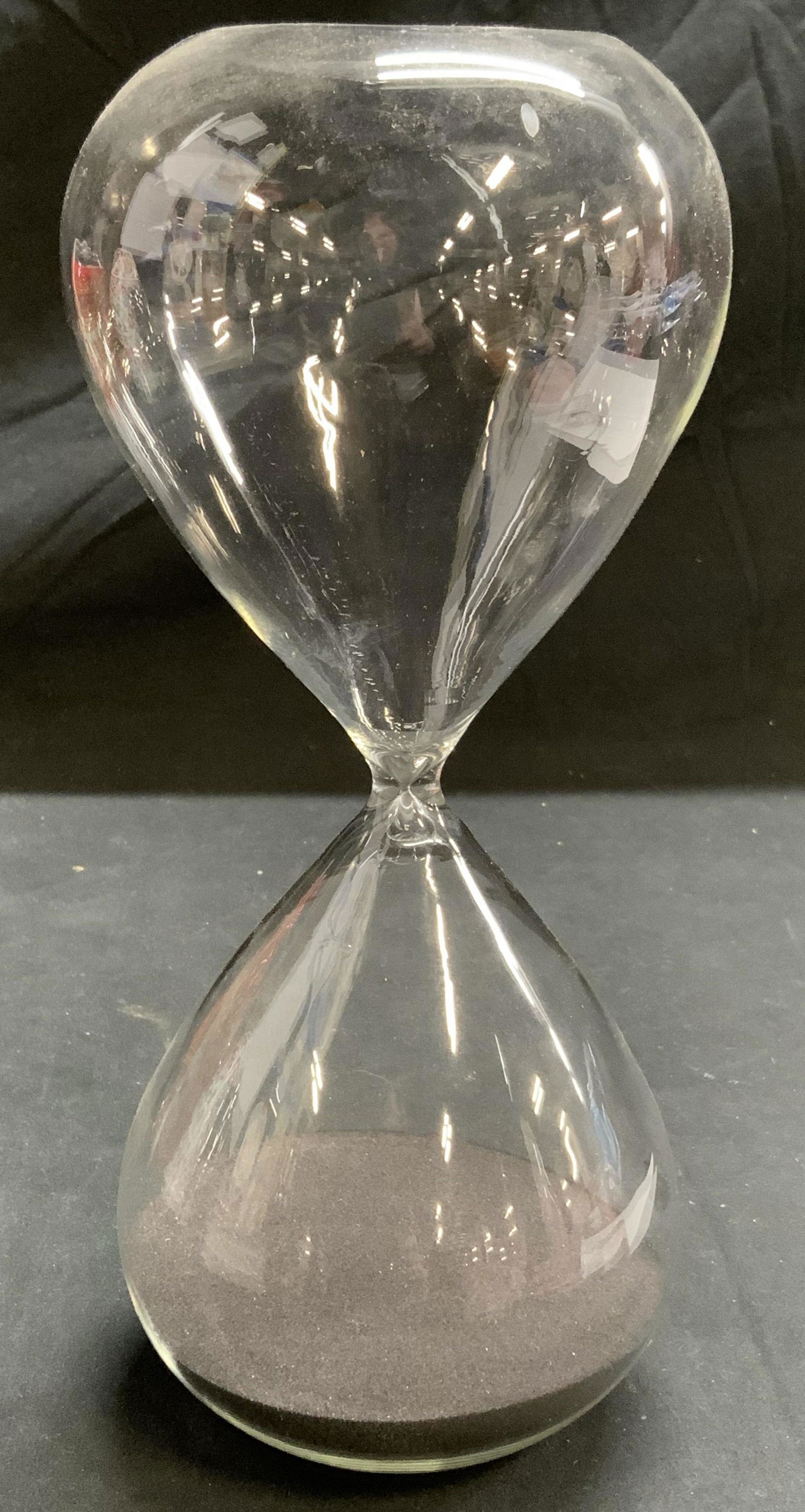 Black Sand Hourglass, Table Accessories: Transparent glass hourglass with black sand. Measures approx. 4.5 inches diameter and 9.5 inches tall. In good condition, minor wear to surface consistent with exposure. Hourglass, black sand hourglas