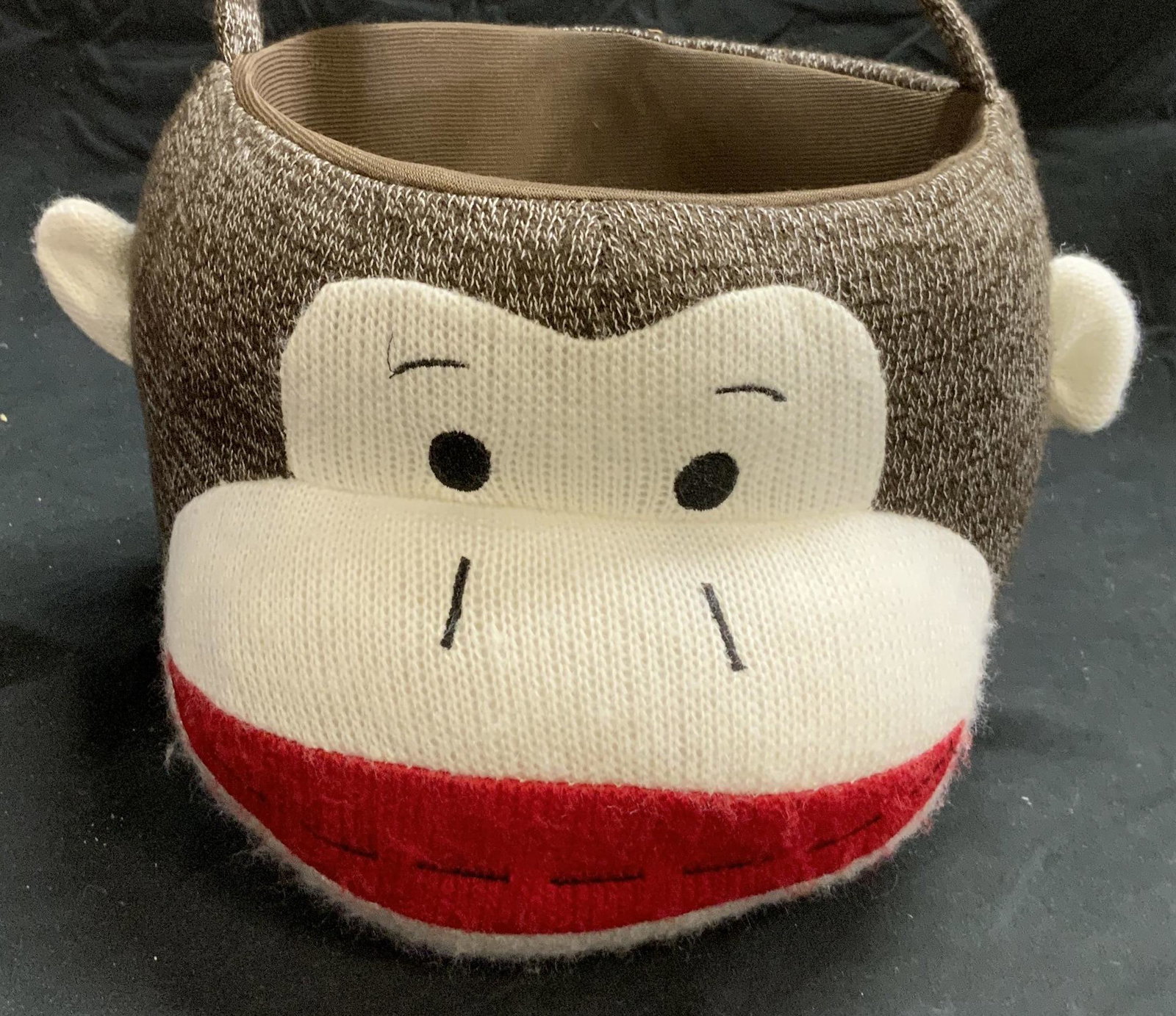SOCK MONKEY Knit Basket: Sock Monkey knit basket in hues of brown, white, and red. Trademarked on tag to underside. Polyester and plastic stiffener. Some wear consistent with exposure. Measures approx. 9 inches diameter and 6