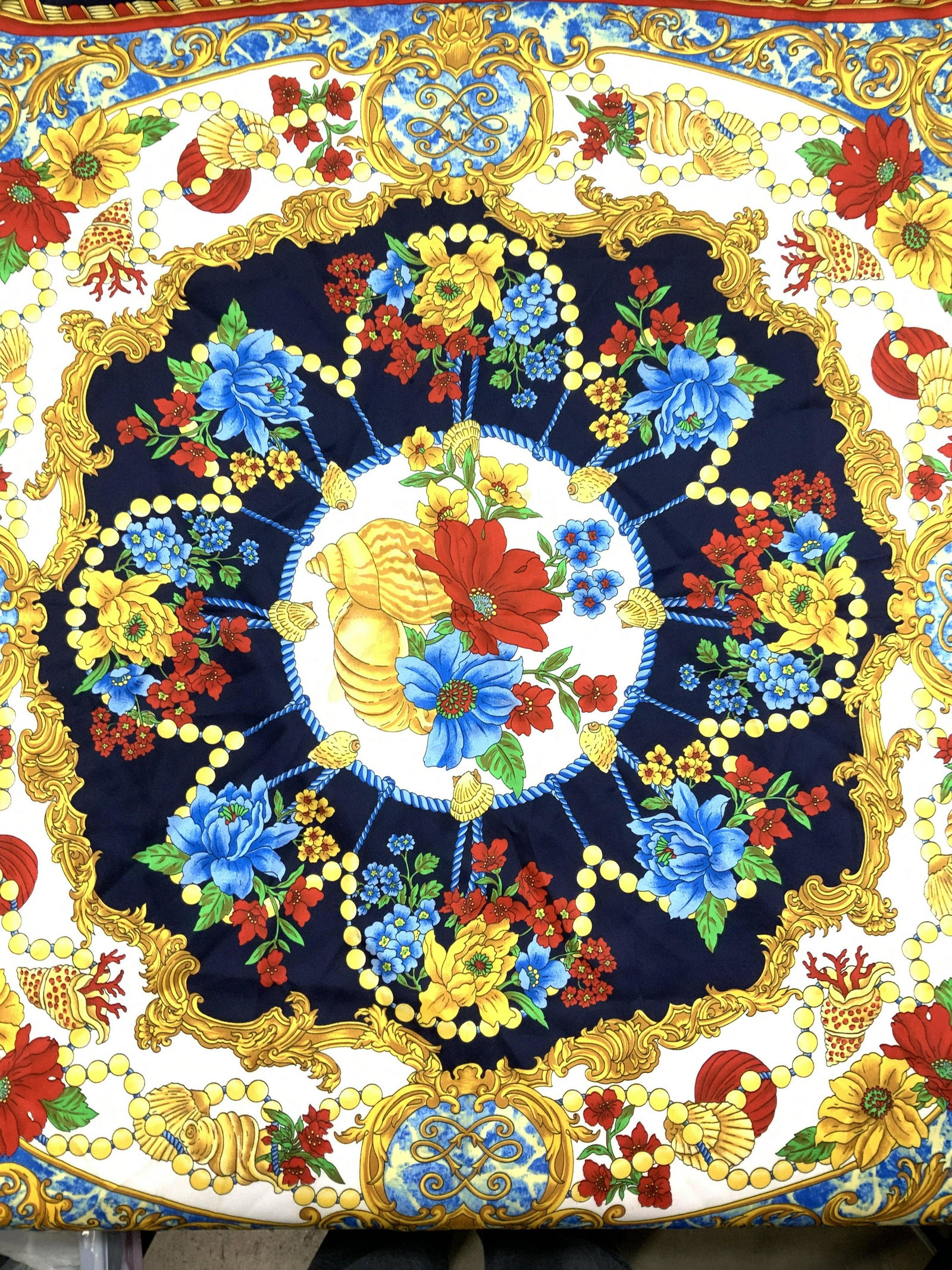 Art of the Scarf Acanthus Venetian Scarf Italy: Brightly colored florals, seashells, and gold Venetian Acanthus scroll and leaf print scarf. Exterior is a dark navy blue with pops of gold, red, and turquoise blue. Made in Italy. 35 x 34.75 in. 100 