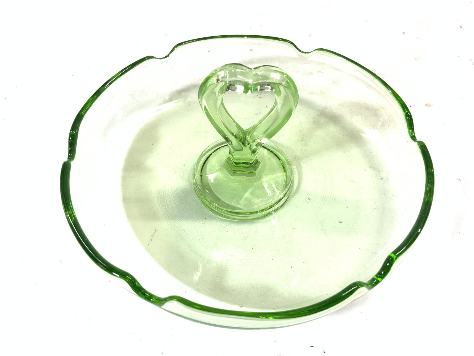 Depression Glass Dip Dish W Heart Handle Green: Piece is green toned glass. Handle in center is heart shaped. Piece has small dips to rim. Piece measures approx 7 inches wide 3 inches tall. Dip dish, Art glass, depression glass, green art glass, de