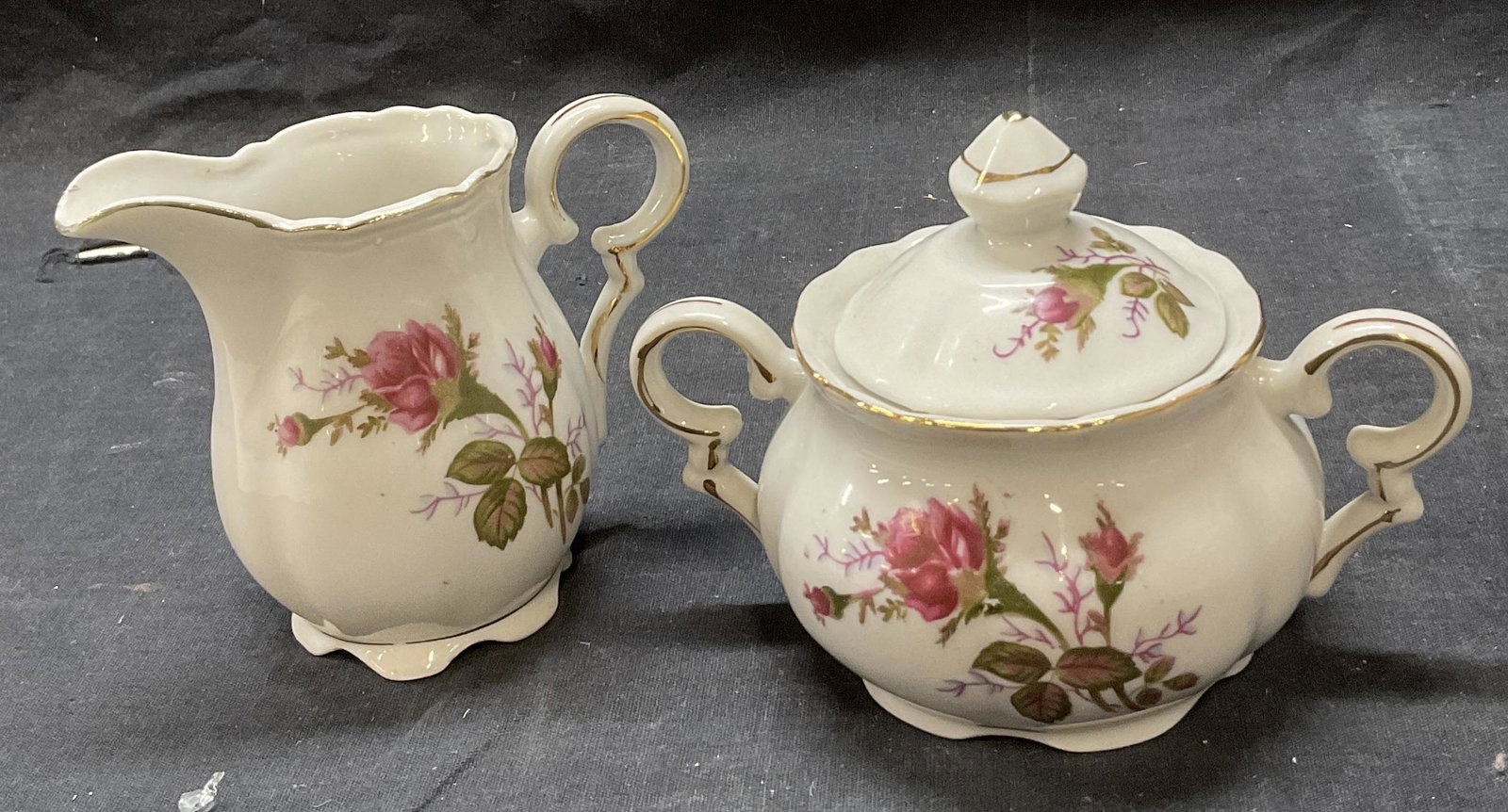 Porcelain Floral Creamer and Sugar Bowl: No markings to bottom. Largest Meade is paper. 5.5 x 3 x 4.25 inches. Gold tone detail to pieces. Rose motif to exterior of piece. No visible chips to pieces. Porcelain ware, porcelain creamer, porcel