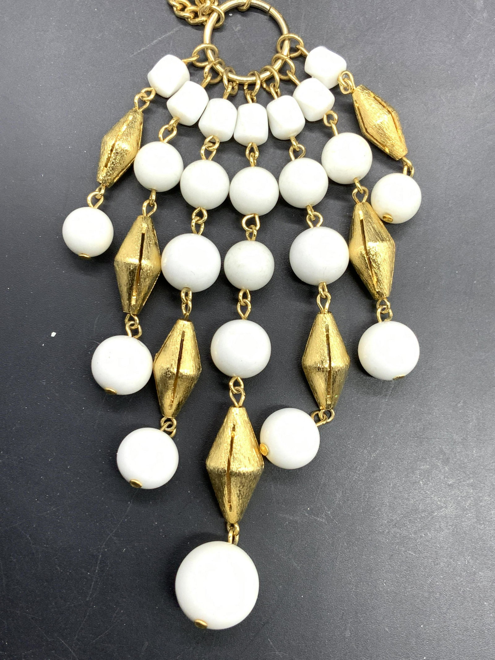 Gold Tn Curd Chain Neck w Bead Tassel Pendant: 31 in. long gold tone curd chain necklace accented with sculptural diamond cut gold tone beads and round white beads. Necklace ends with a beaded tassel pendant, 4 in long, 2.5 in wide, contrasting 24