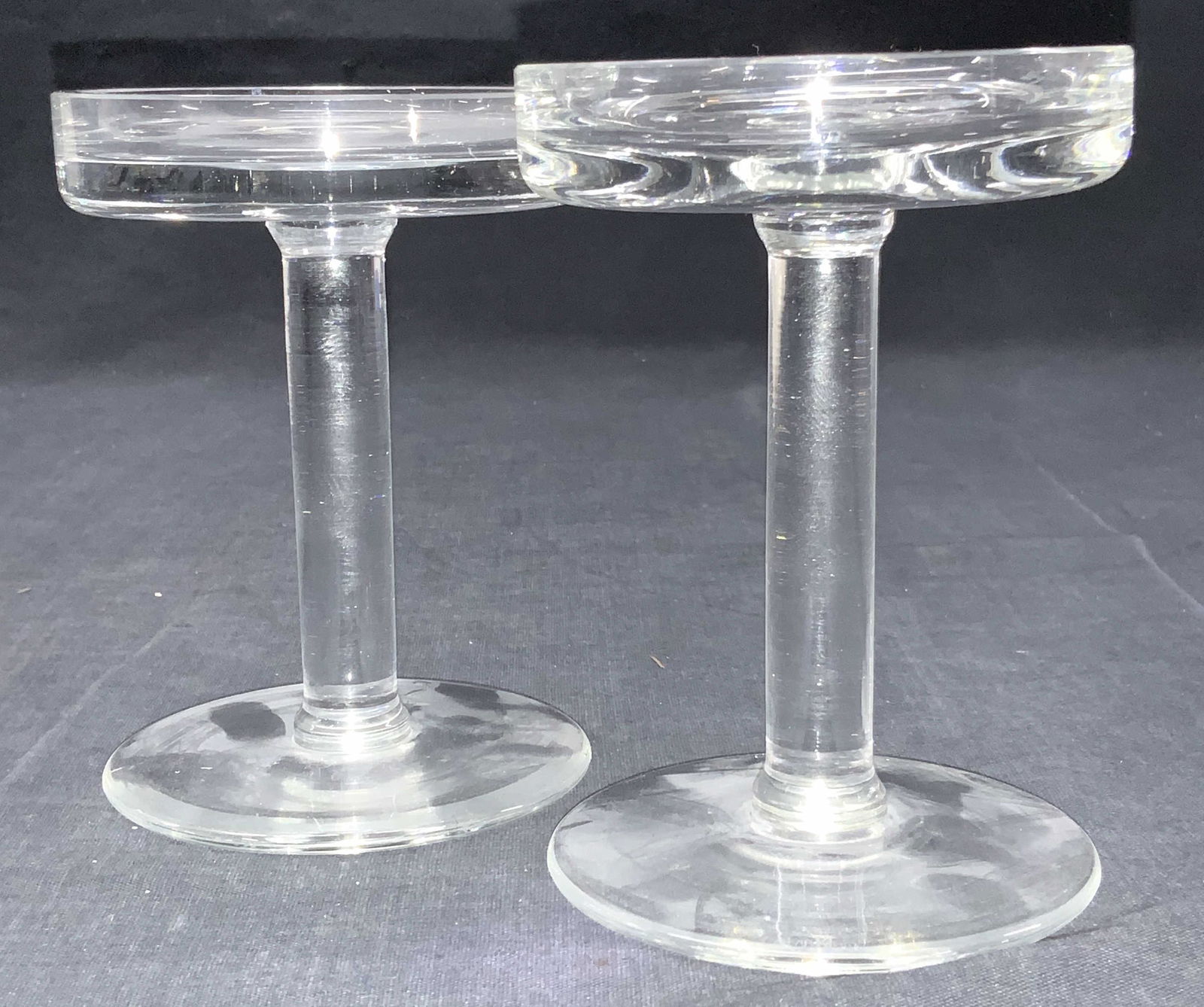 CALVIN KLEIN Crystal Pedestal Candle Holders: Marked Calvin Klein on undersides. Pair of crystal pedestal candle holders with clear stems and shallow tops. Approximately 5 to 4.75 inches tall. 1 slightly taller than the other. Condition is consis