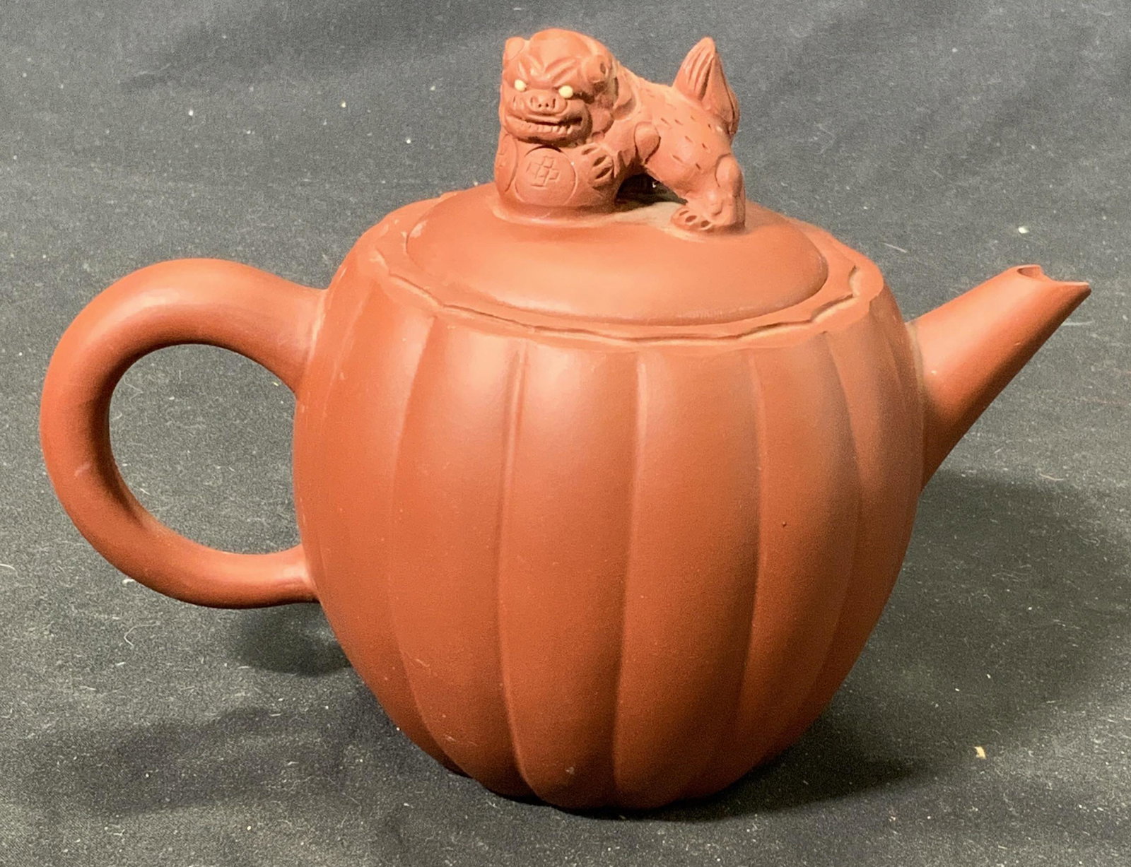 YIXING Signed Chinese Pottery Guardian Lion Teapot: Yixing pottery red clay teapot with guardian lion motif on lid. Stamped with Asian character signature to underside. Chipping to inner lip and spout. Measures approx. 7.25 inches wide and 5.25 inches 