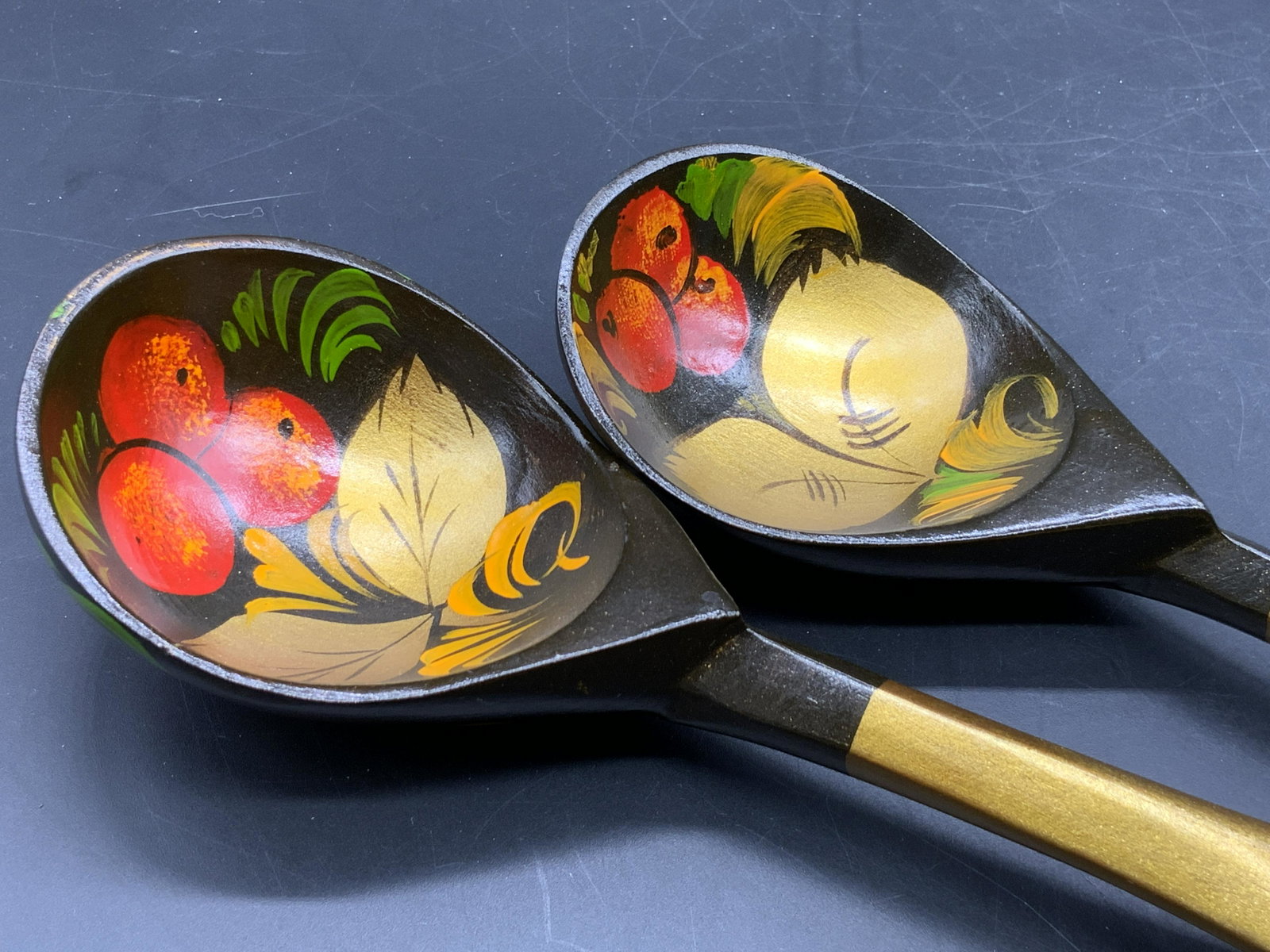 Pair Vintage Handmade Russian Khokhloma Spoons: Handmade and hand painted wooden Russian Khokhloma spoons. Primarily red, gold, green, and deep brown hues. Berry motif to the spoons. Measures approx 9.5L x 2.5W in. Some losses present, some wear co