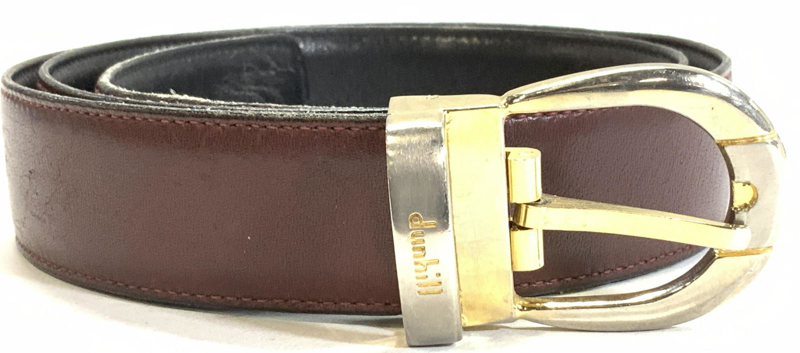 DUNHILL Burgundy Leather Belt: Signed Vintage Dunhill Leather belt, exterior is burgundy leather, underside is black leather. Horseshoe shape belt buckle in gold tone ( some wear to color). Belt measures 38.5 x 1.25 in. L x W, 5 pr