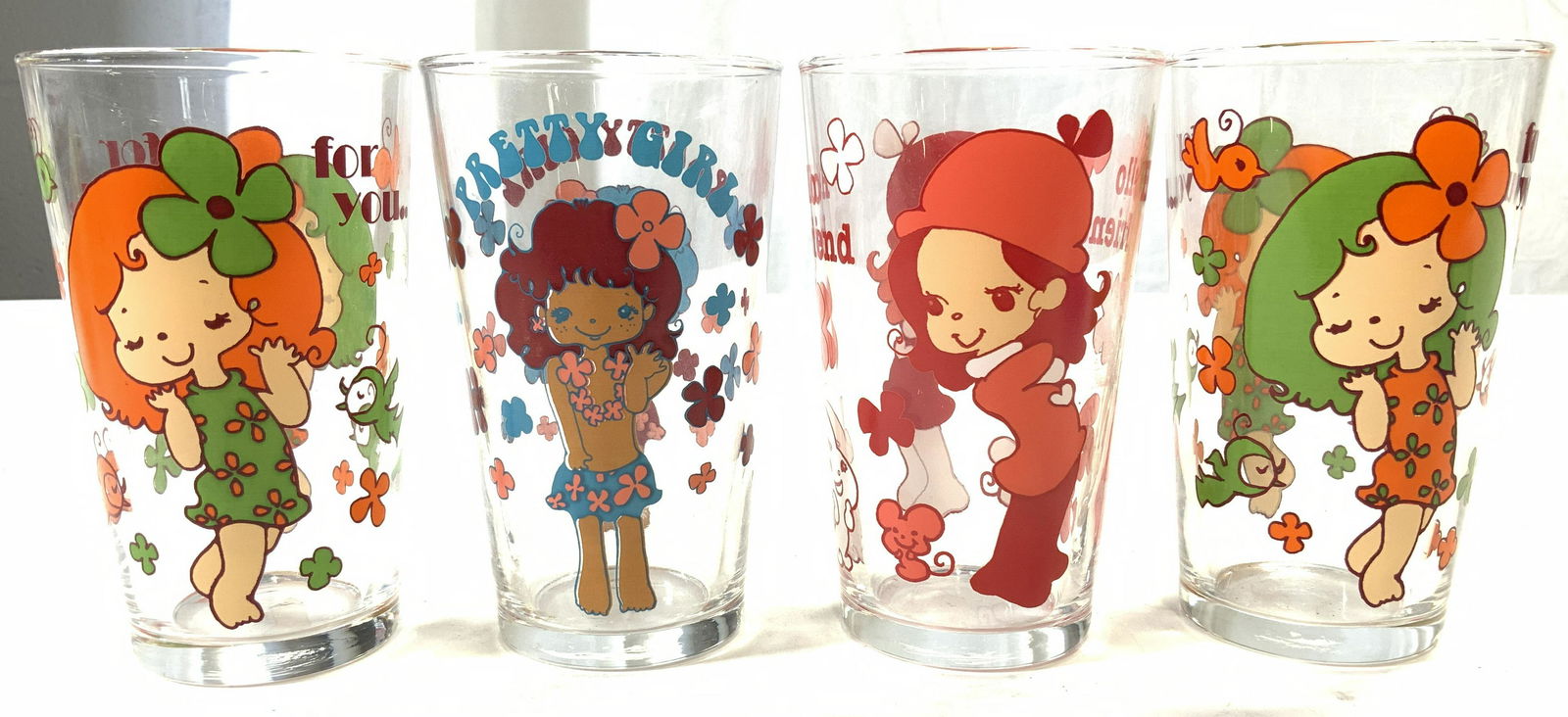 Lot 4 Glass Vessels W Illustrated Female Figures: Lot includes 4 glass vessels. Each have various illustrated female figures with text such as PRETTY GIRL, FOR YOU, & HELLO FRIEND. Each cup has floral detail. Each measures approx 4.25 inches tall 2.5